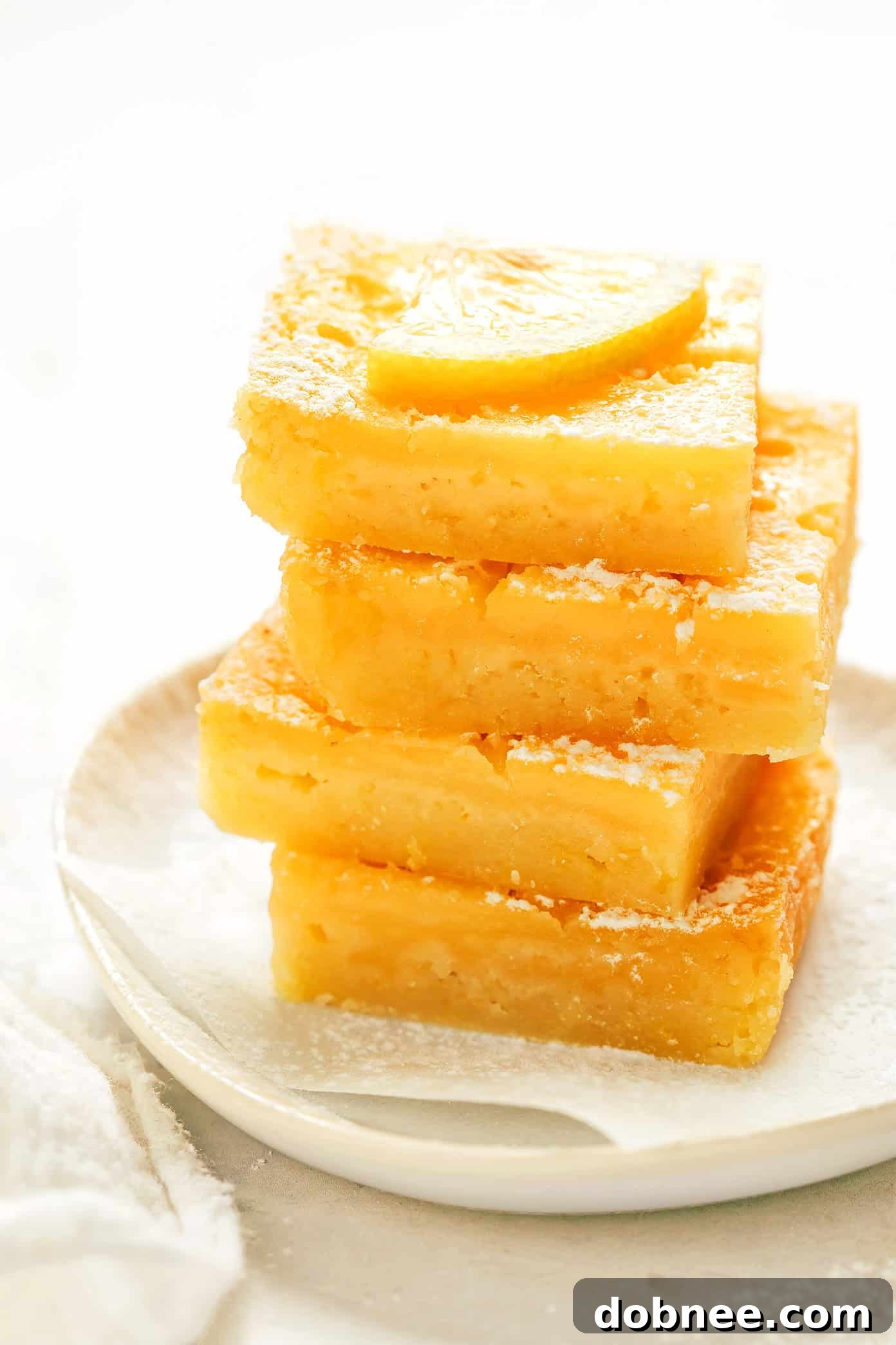 A close-up shot of a slice of lemon bar, showing the distinct layers of crust and filling, garnished with a thin lemon slice.
