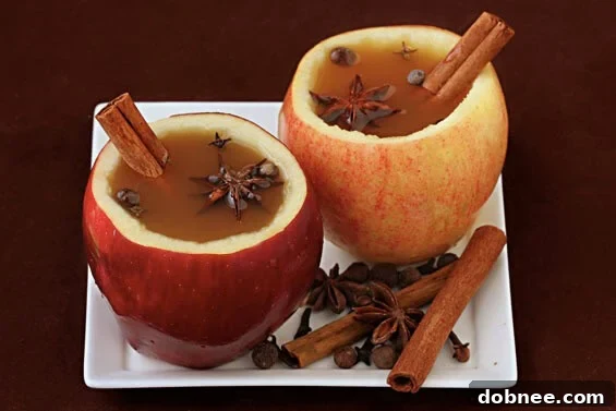 Two beautifully crafted apple cider cups filled with warm cider and garnished with cinnamon sticks, set against a rustic background.