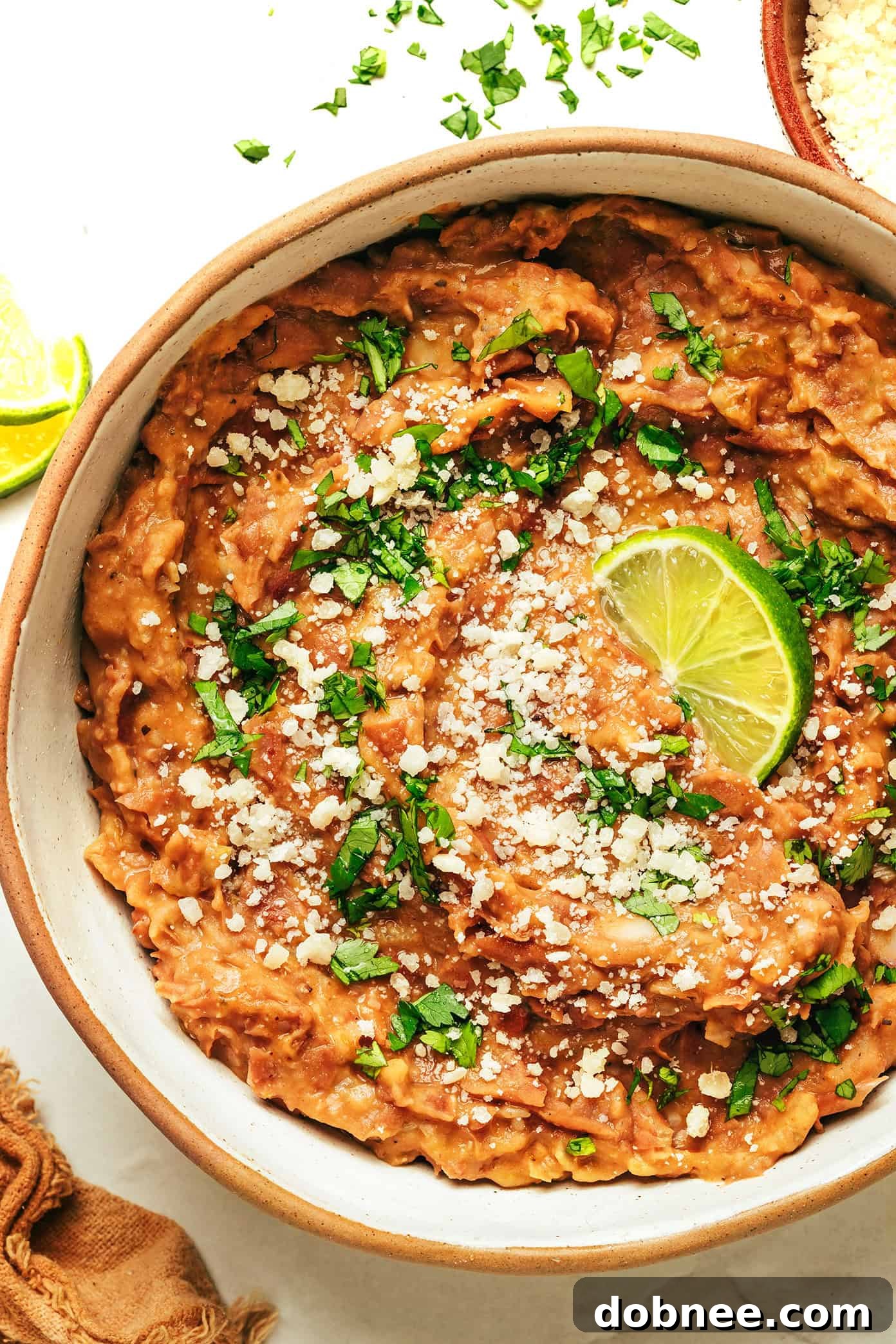 A vibrant bowl of homemade refried beans, garnished with fresh cilantro and a lime wedge, ready to be served.