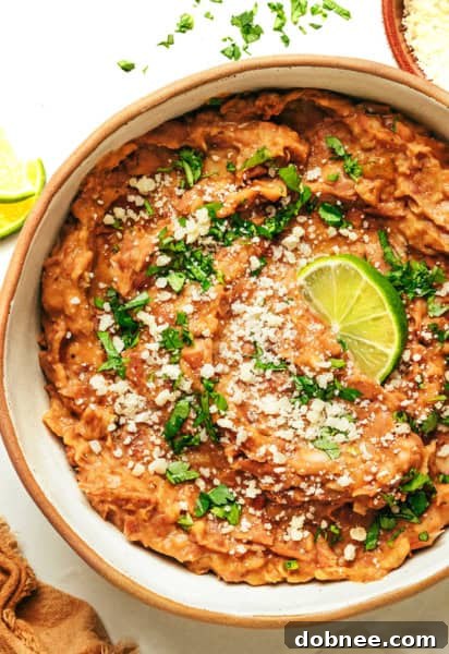 A bowl of delicious homemade refried beans, garnished with fresh cilantro and a lime wedge.