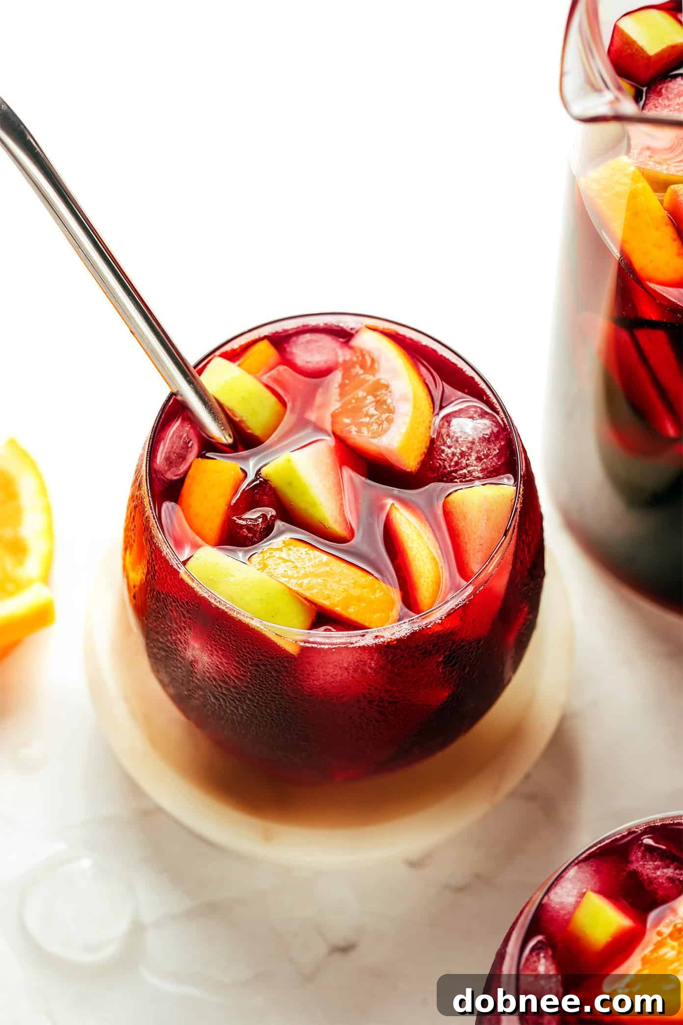 A beautifully presented pitcher of authentic Spanish Sangria, brimming with fresh orange, lemon, and apple slices, perfect for a refreshing summer drink.