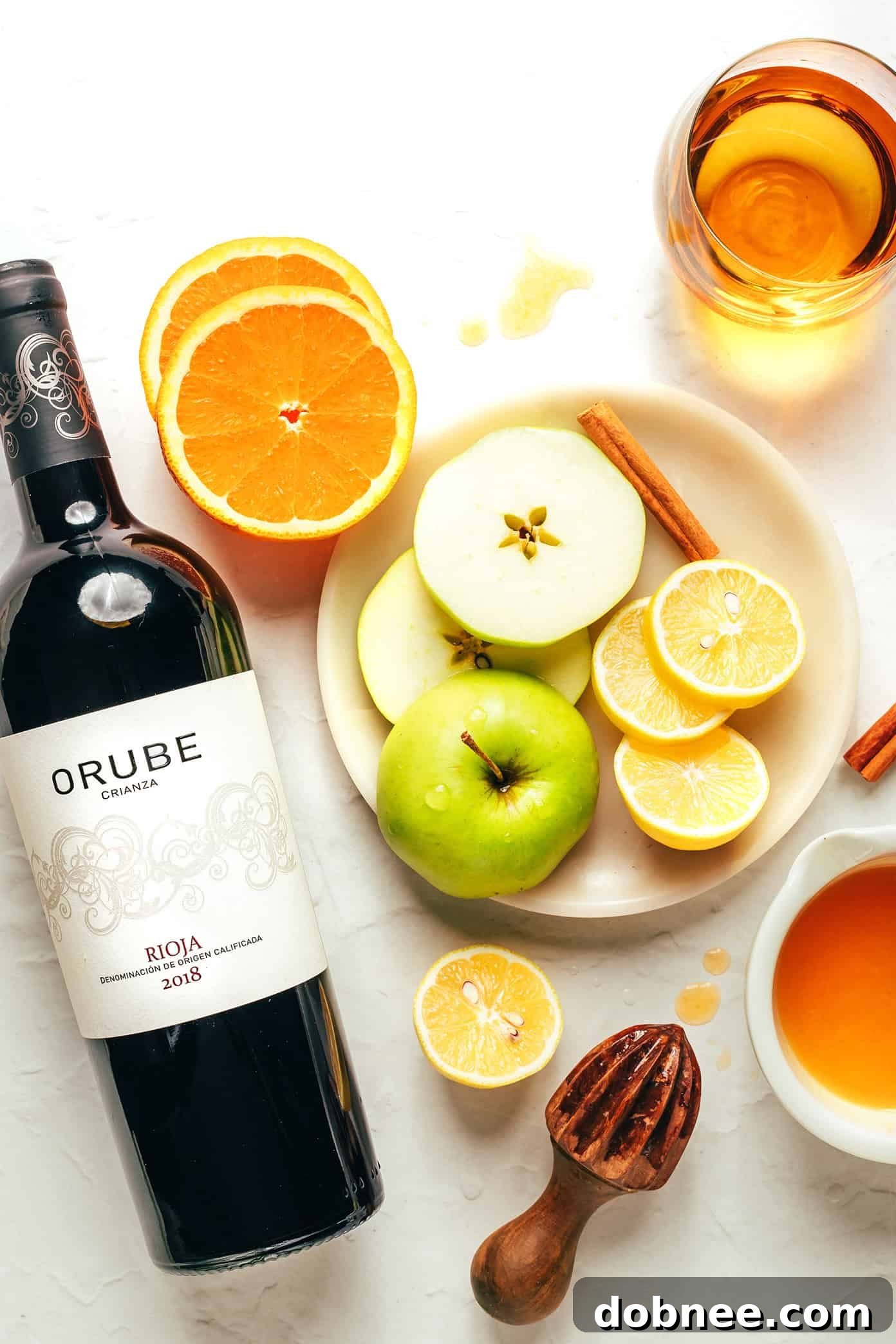 A close-up shot of fresh, vibrant fruit slices, including oranges, lemons, and green apples, being carefully placed into a pitcher of red wine, highlighting the start of the sangria-making process.