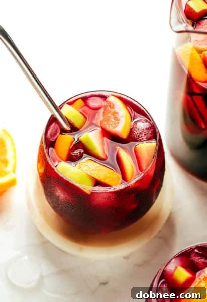 A pitcher of authentic Spanish Sangria alongside two filled glasses, adorned with fresh fruit and ice, ready to be served.