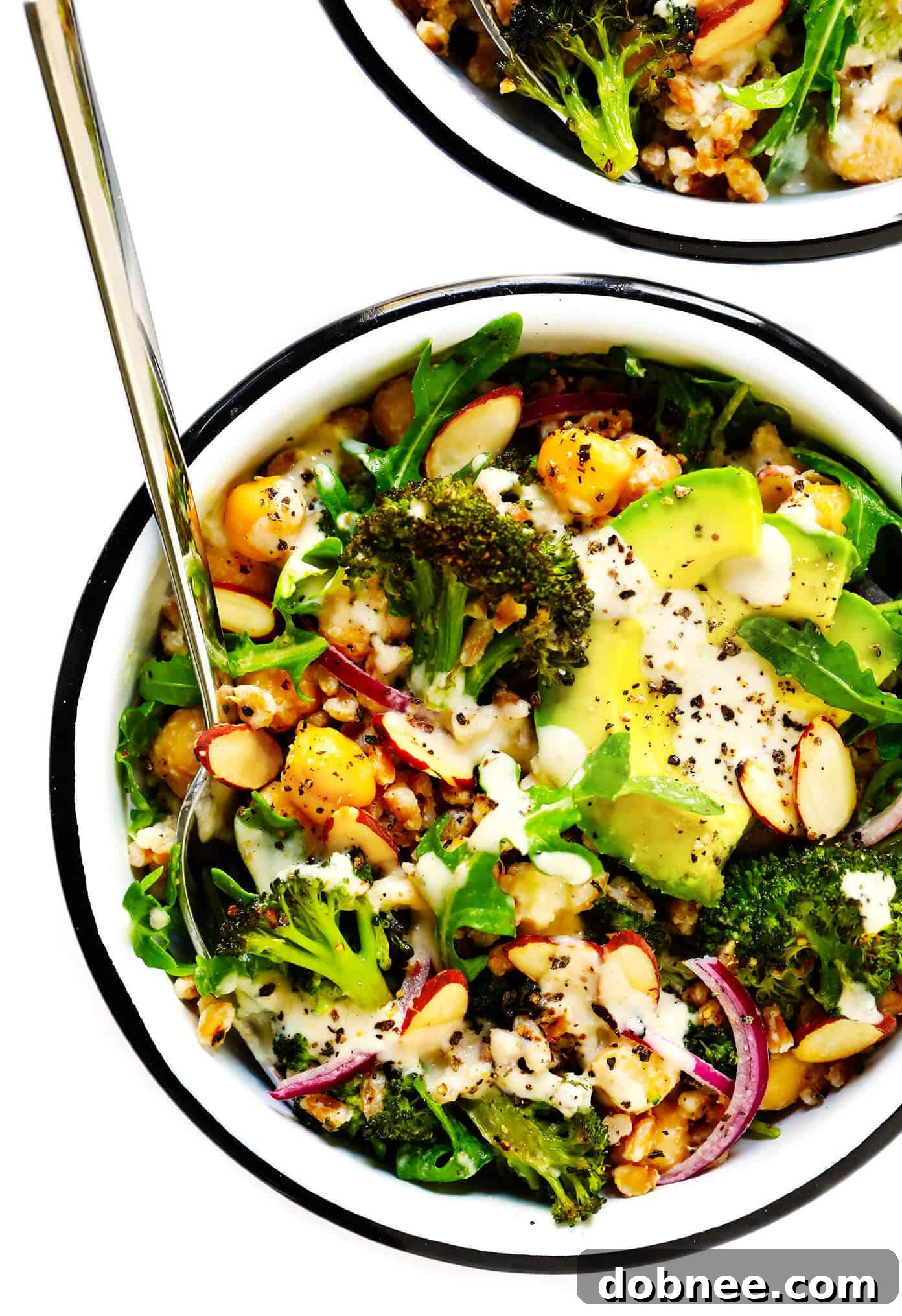 Roasted Broccoli and Farro Bowls, a healthy vegan meal prep recipe featuring avocado, chickpeas, arugula, red onion, and toasted almonds with a dreamy tahini dressing. Perfect for dinner or lunch.