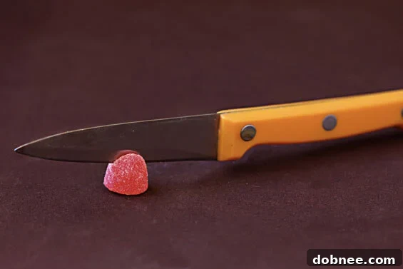 Careful Gumdrop Incision A sharp knife making a precise, angled cut into the top of a colorful, sticky gumdrop to create a stable slot for a place card holder.