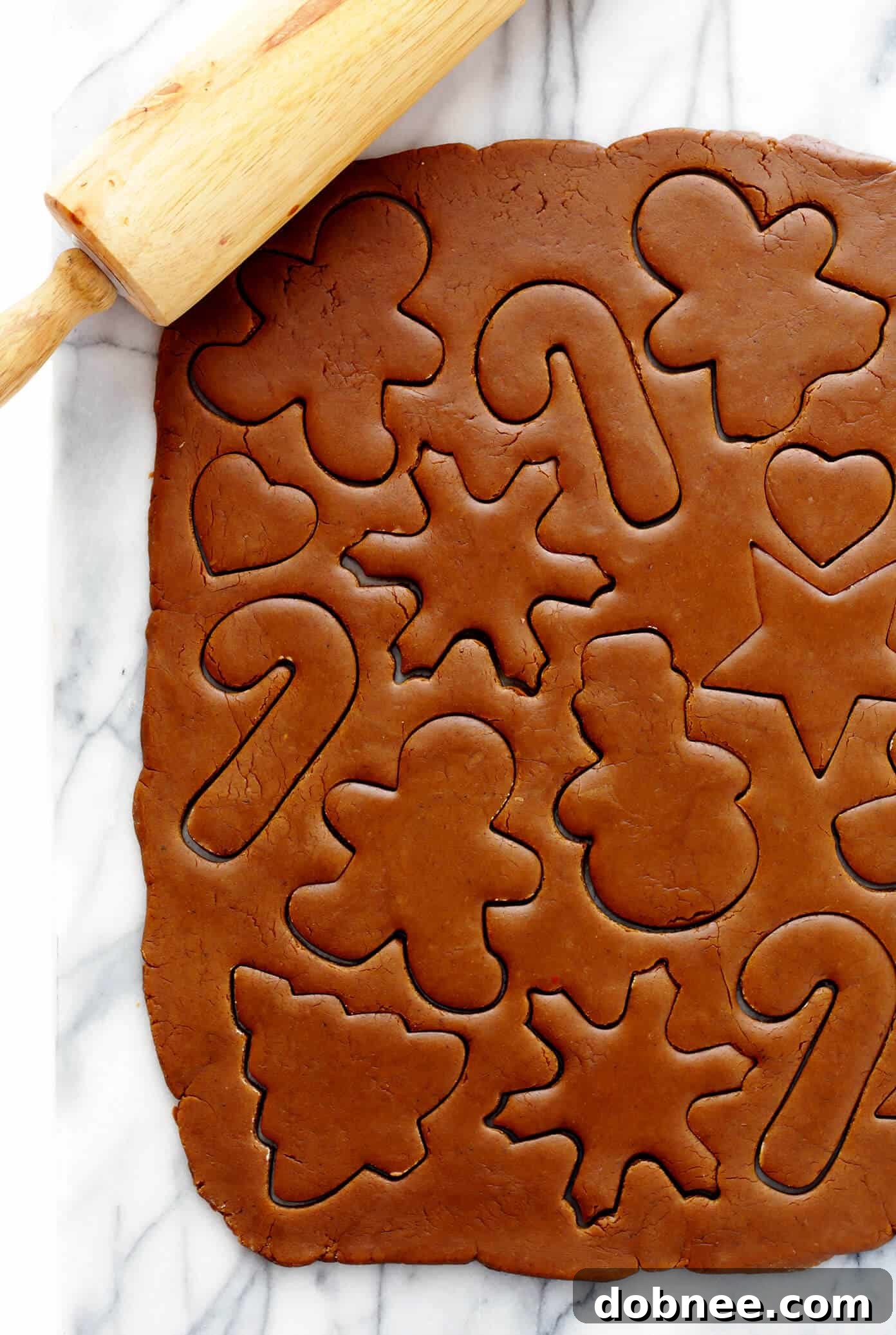Rolling and cutting gingerbread cookie dough on a floured surface.