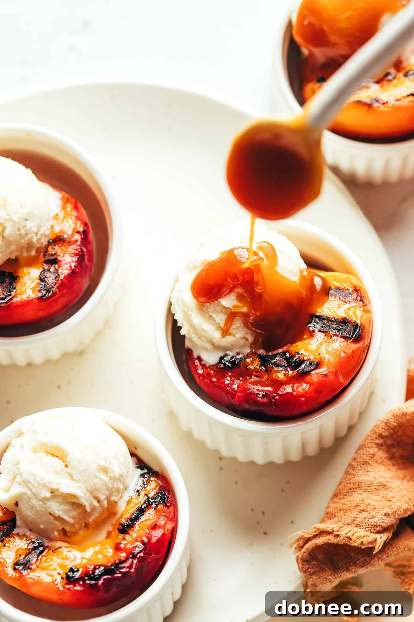 Five grilled peach halves with grill marks arranged on a plate.