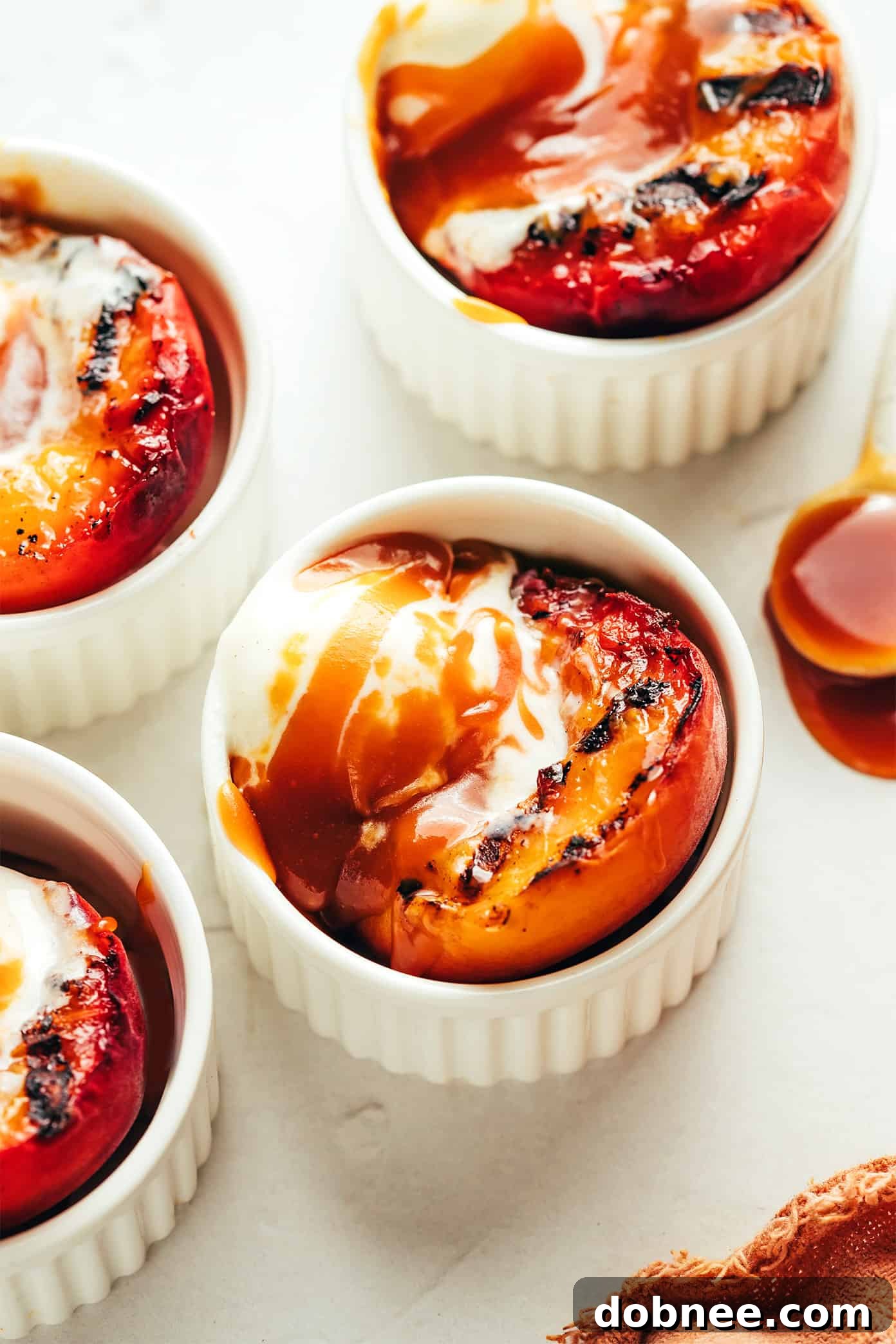 A bowl of grilled peaches with ice cream and bourbon caramel sauce, garnished with fresh mint.