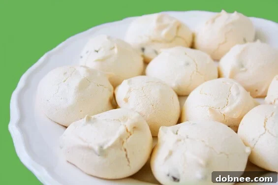 A close-up shot of several freshly baked chocolate chip meringue cookies, showing their delicate cracks and golden hue, arranged on a baking sheet.