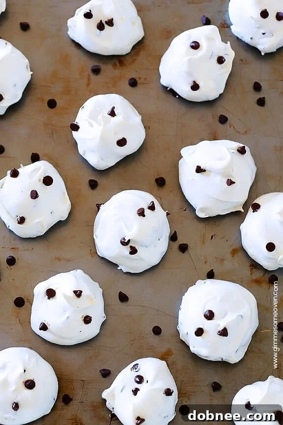 A cluster of beautifully baked chocolate chip meringue cookies, golden and perfectly crispy, piled invitingly on a white plate.