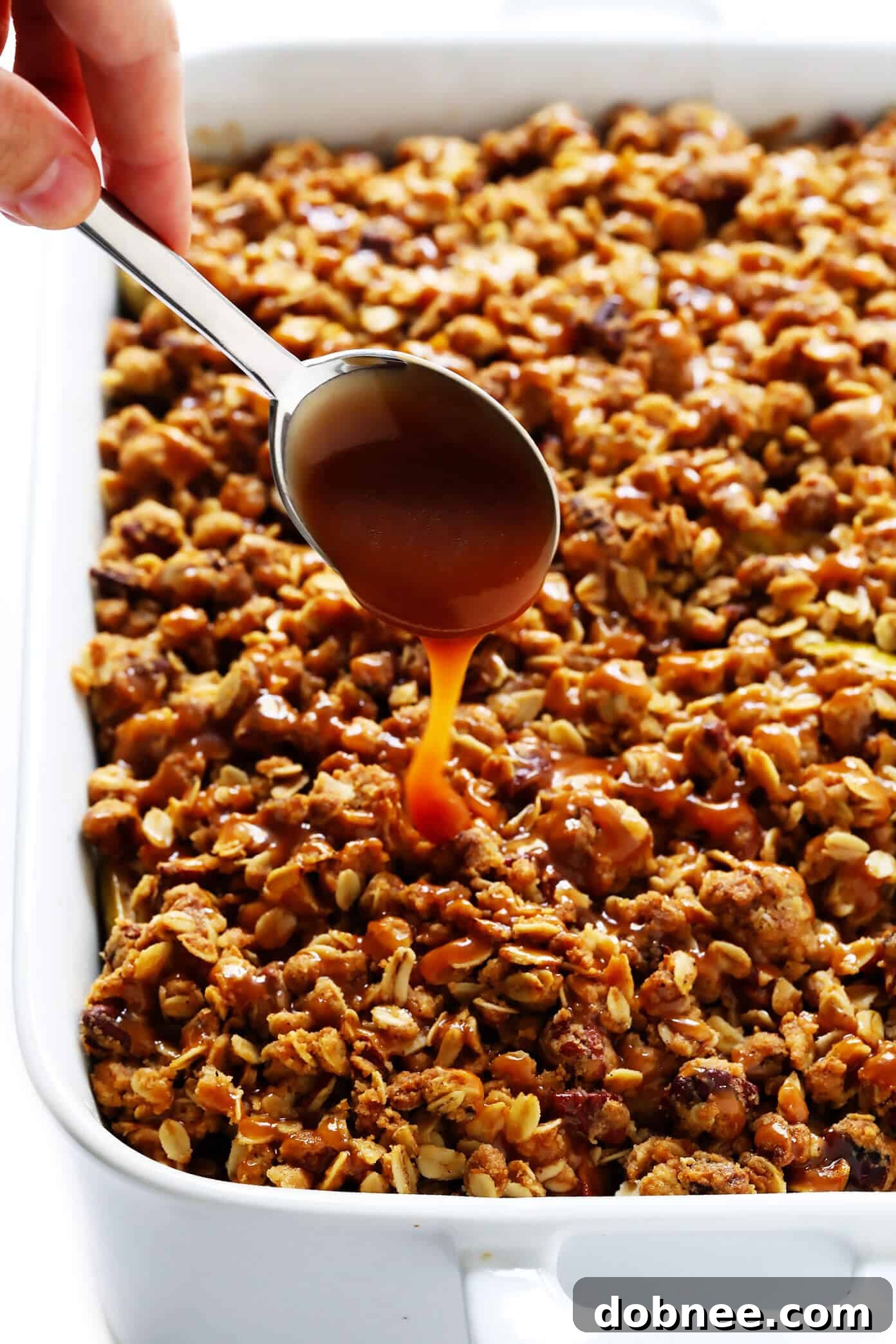A warm, bubbly apple crisp drizzled with caramel sauce, ready to be served.