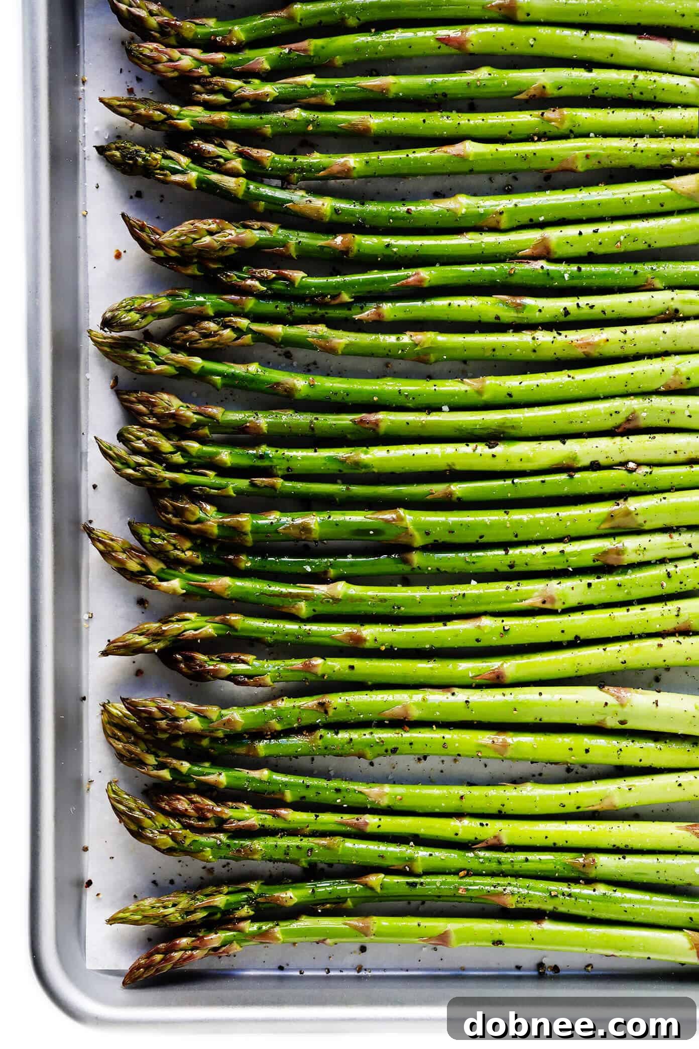 A baking sheet lined with parchment paper, topped with neatly arranged, raw asparagus spears drizzled with olive oil and seasoned with salt and pepper, ready for roasting.