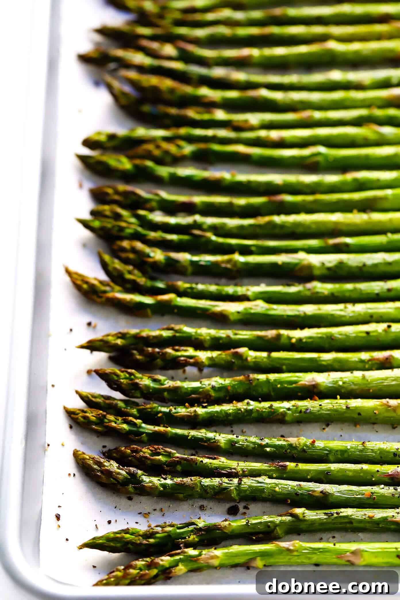 Close-up of freshly oven roasted asparagus spears on a white plate, ready to be served, showcasing their vibrant green color and tender-crisp texture.