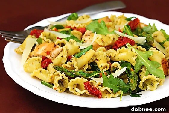 Pesto pasta with chicken, asparagus, and arugula in a white bowl, garnished with parmesan cheese.