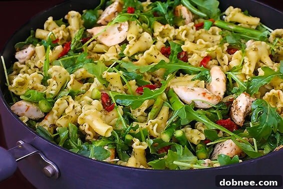 Close-up of pesto pasta with chicken, asparagus, and arugula, showing the vibrant colors and rich sauce.