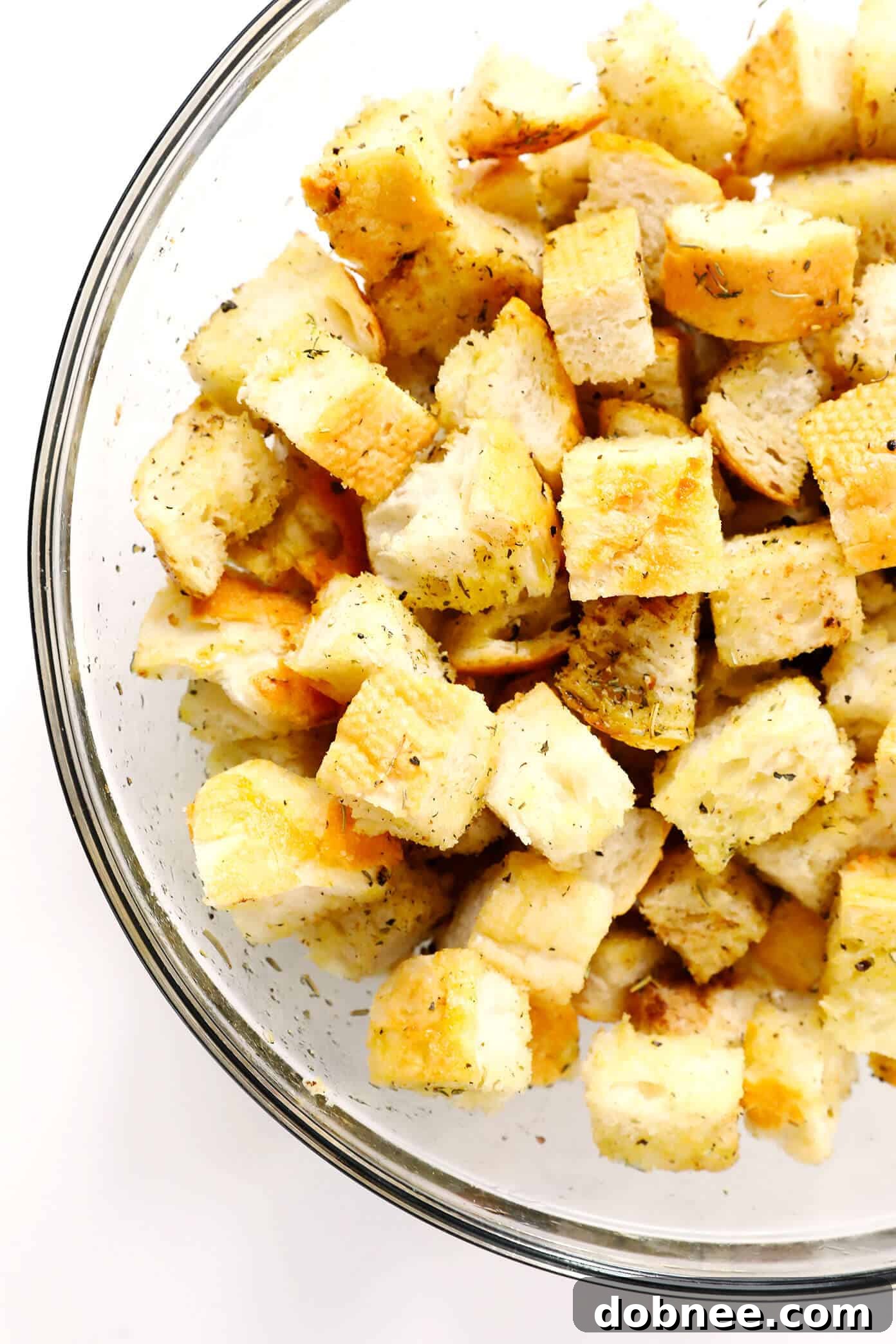 How To Make Homemade Croutons - Close-up of bread cubes being tossed with olive oil and seasonings in a large mixing bowl.