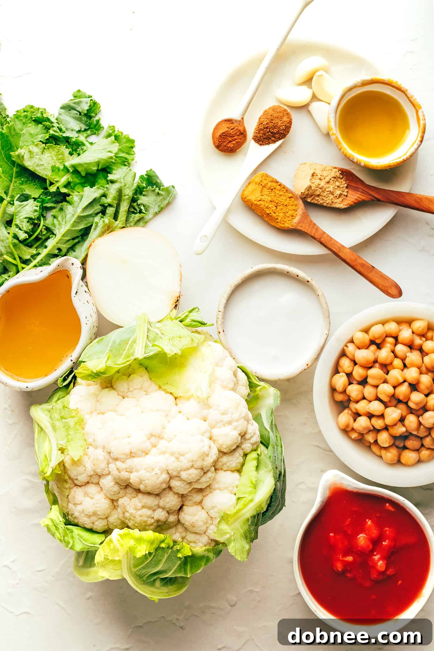 Heartwarming Cauliflower Curry 3 Fresh ingredients laid out for making cauliflower curry, including a head of cauliflower, kale, and spices.