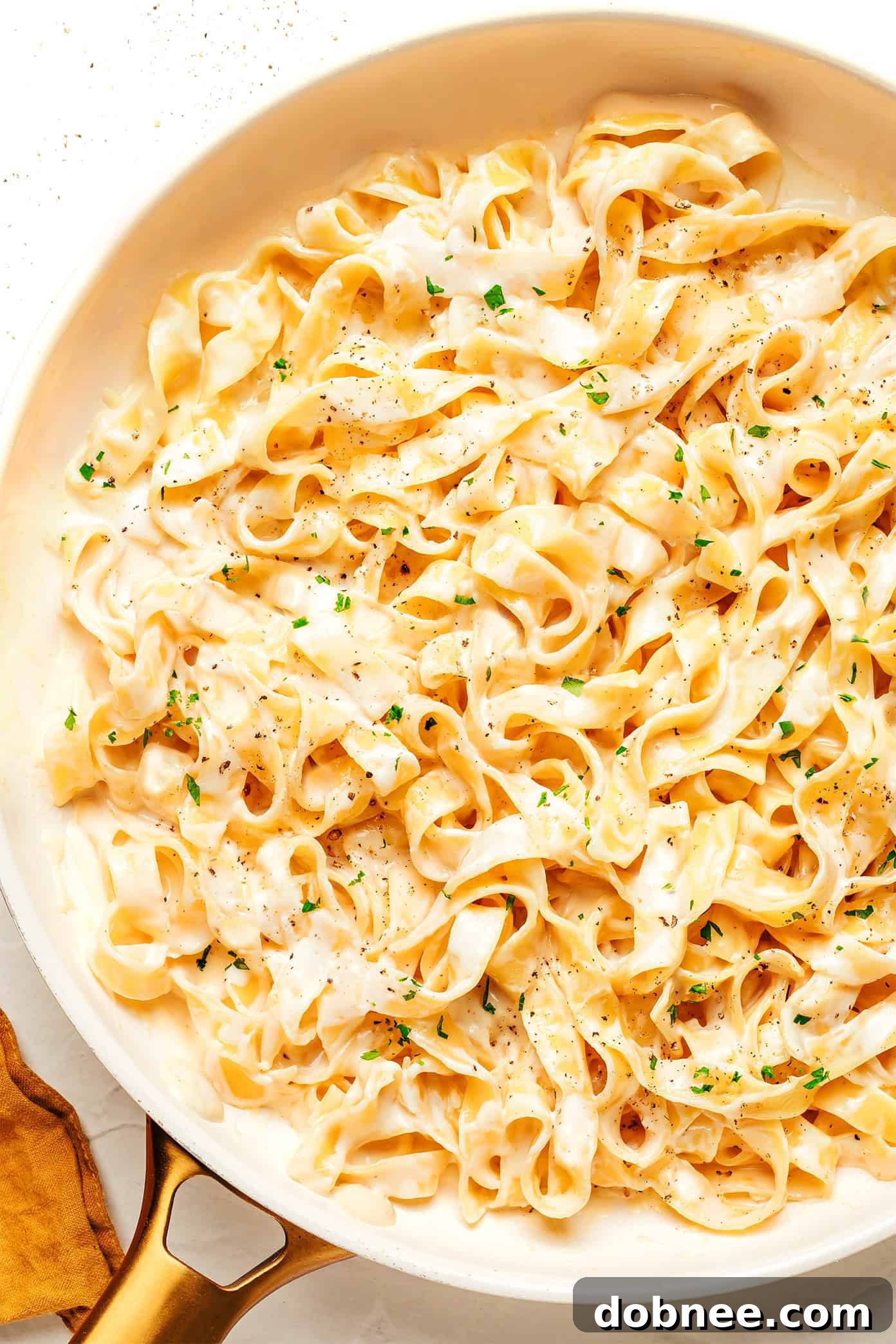 A close-up of delicious Alfredo sauce mixed with fettuccine pasta, garnished with fresh herbs.
