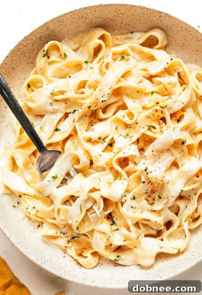 A bowl of creamy Alfredo sauce, garnished with fresh herbs, alongside a wooden spoon.