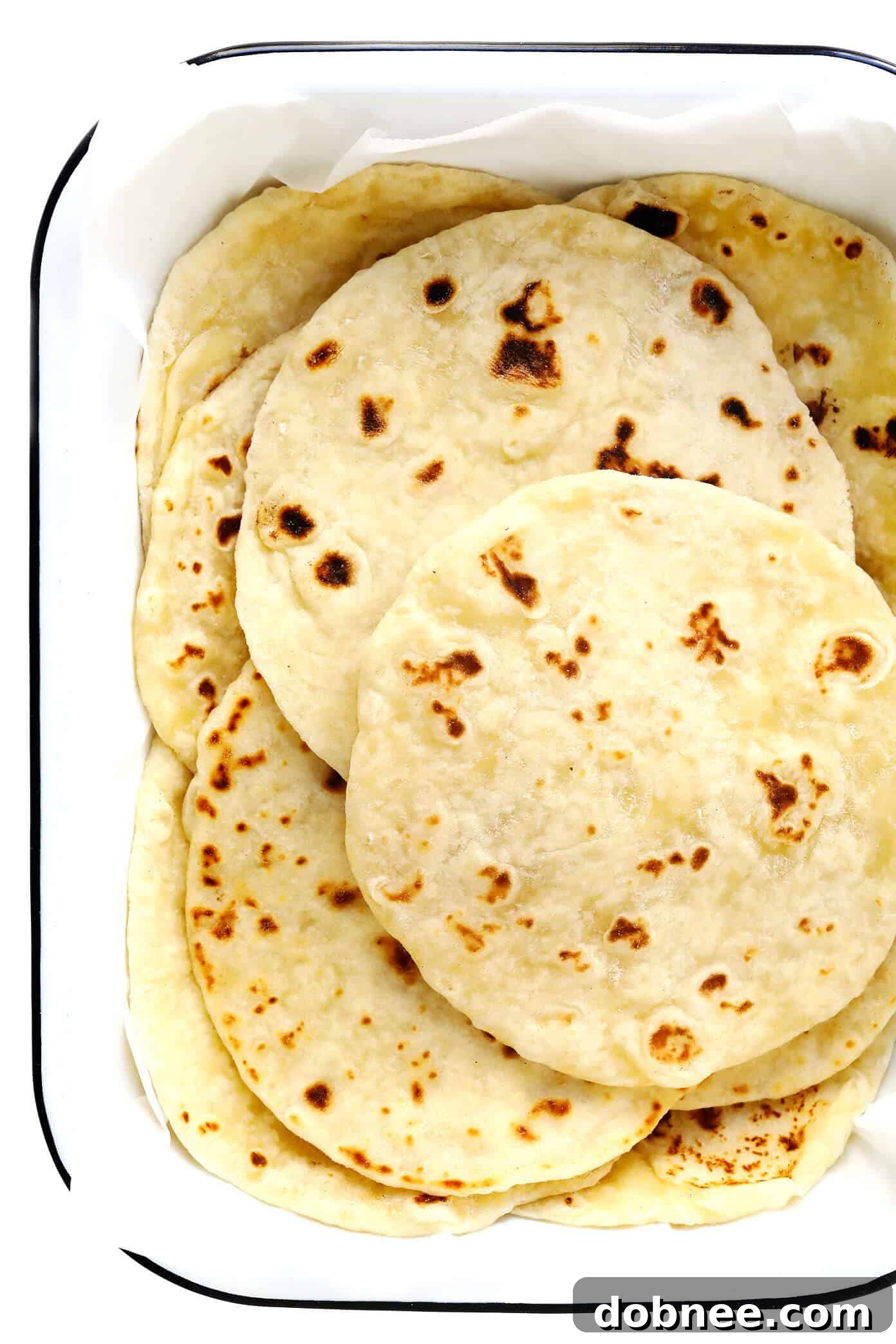Freshly made homemade flour tortillas stacked high on a wooden cutting board.
