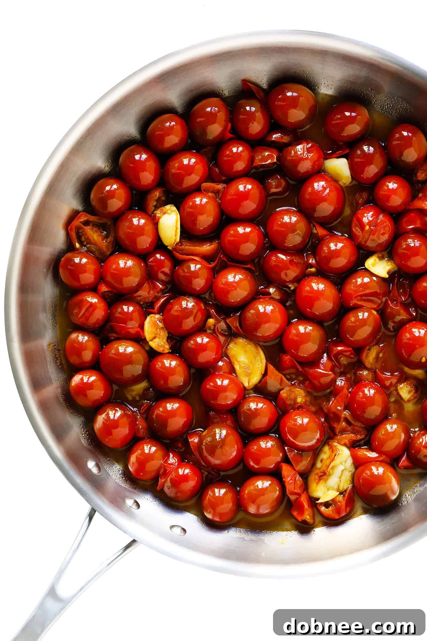 Close-up of a vibrant burst cherry tomato sauce simmering with garlic and olive oil, forming the rich base for pasta