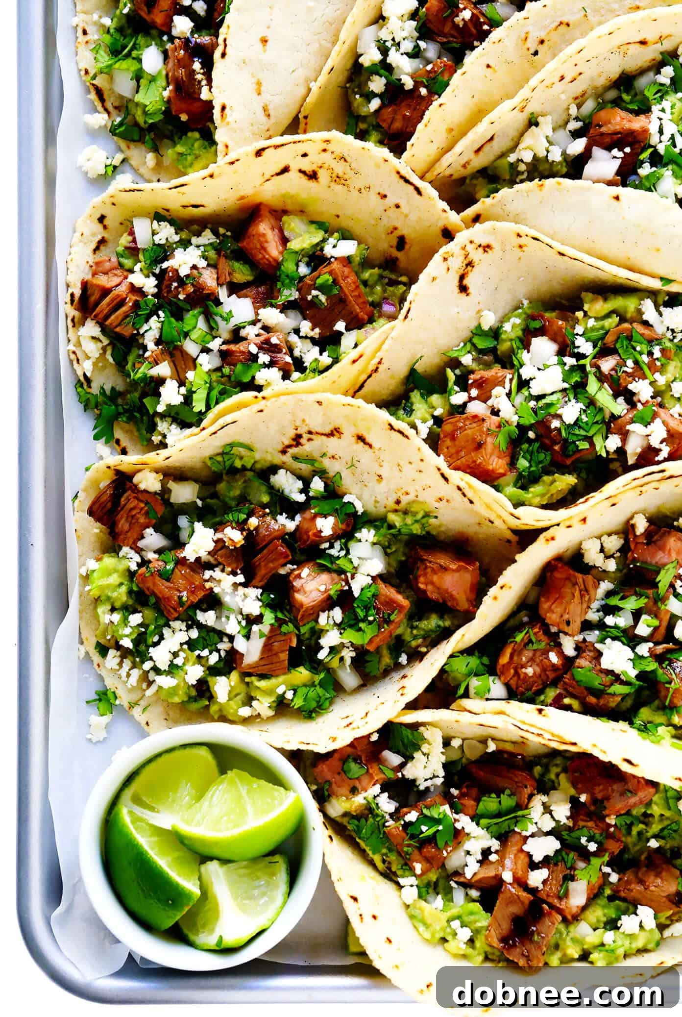 My favorite recipe for street-style Mexican carne asada tacos -- made with tender marinated grilled steak, soft corn tortillas, guacamole or sliced avocado, and whatever other toppings sound good! | gimmesomeoven.com #carneasada #beef #steak #tacos #mexican #avocado #guacamole #glutenfree #dinner Tray of Carne Asada Tacos with Lime, Guacamole and Queso Fresco