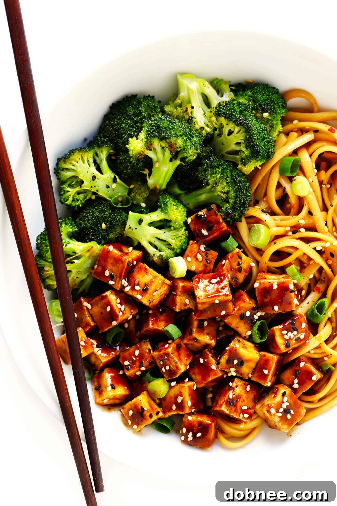 Five Spice Tofu with Sesame Noodles served in a bowl, garnished with green onions and sesame seeds, alongside roasted broccoli.