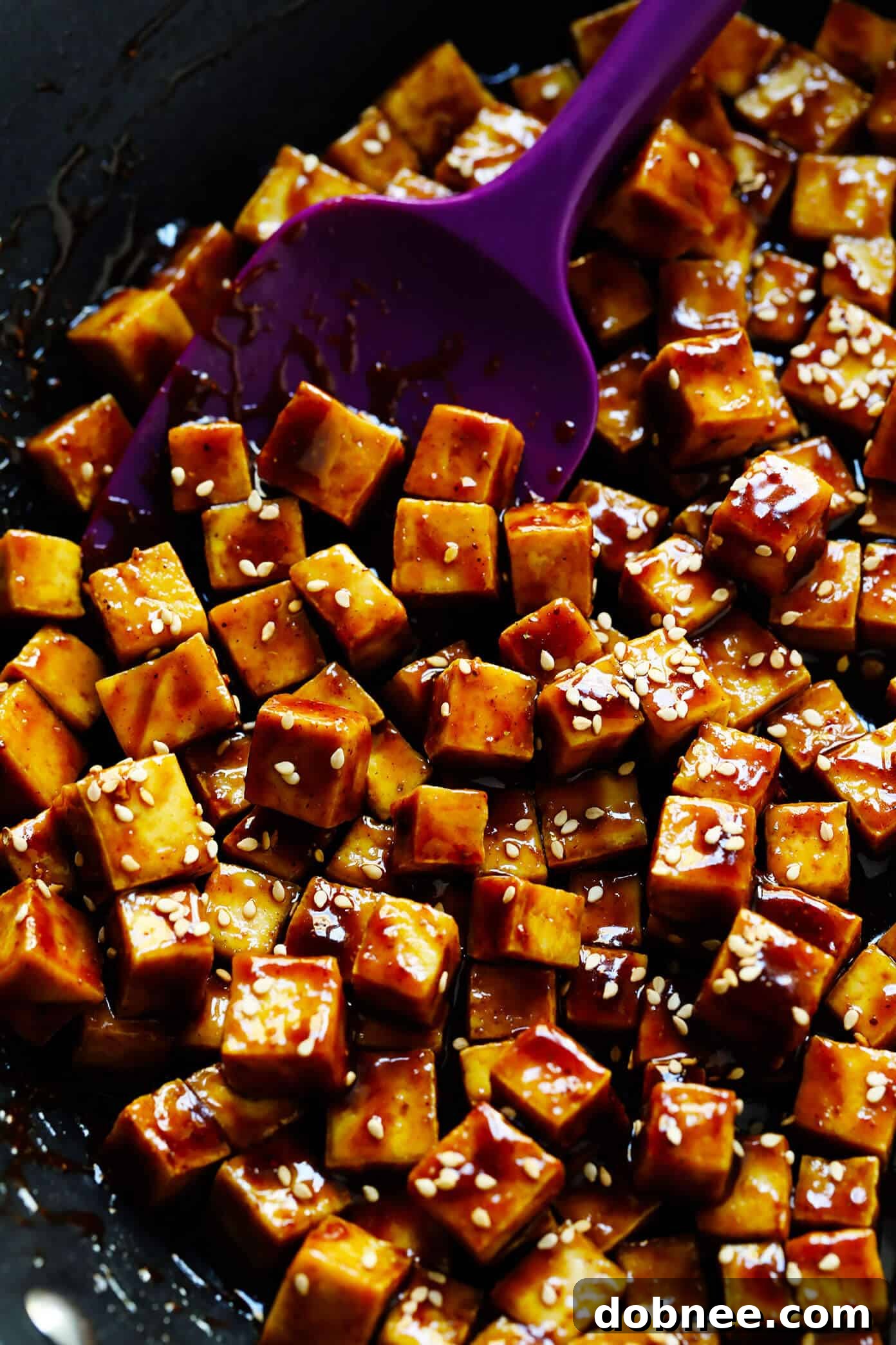 Crispy Tofu is being sautéed in a non-stick pan, then tossed with the rich five-spice hoisin sauce.