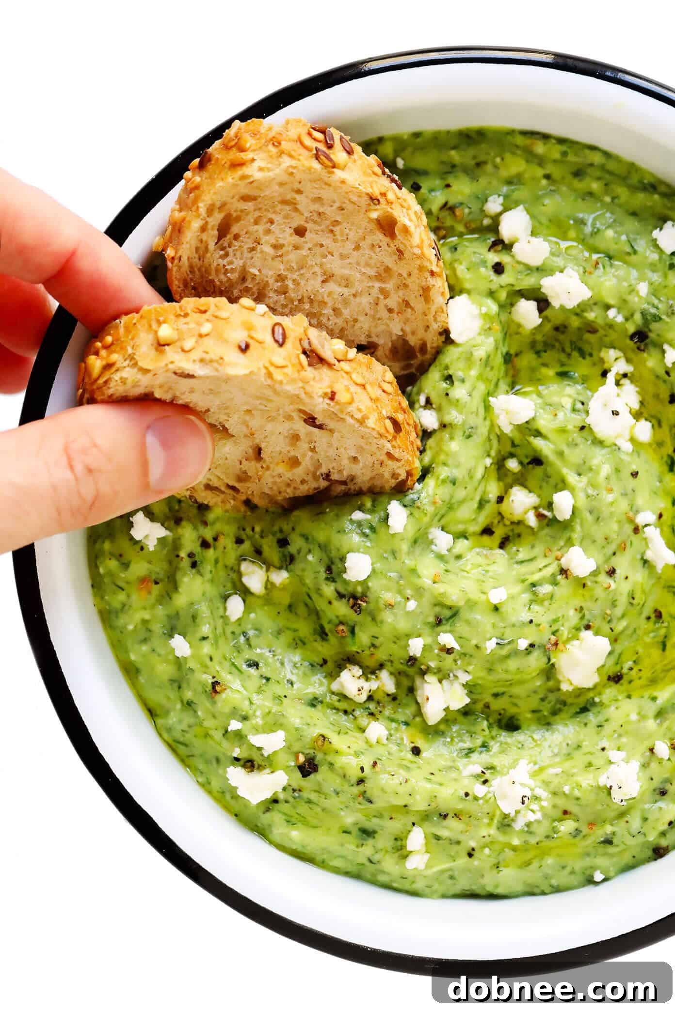 A bowl of Green Goddess Feta Dip surrounded by various dippers, including bread and vegetables.