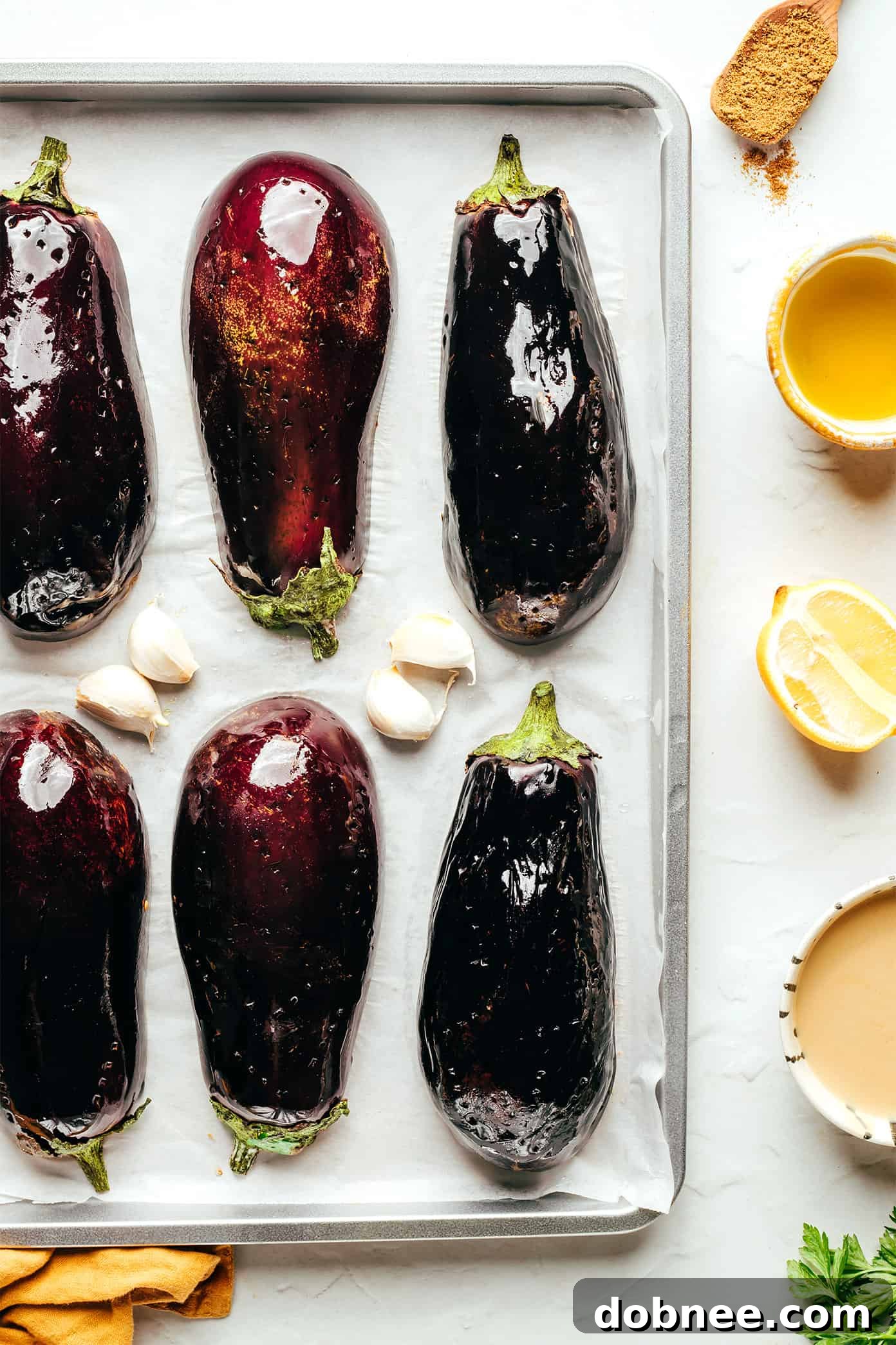 All the ingredients for baba ganoush laid out on a table, including roasted eggplant, tahini, lemon, garlic, and spices.