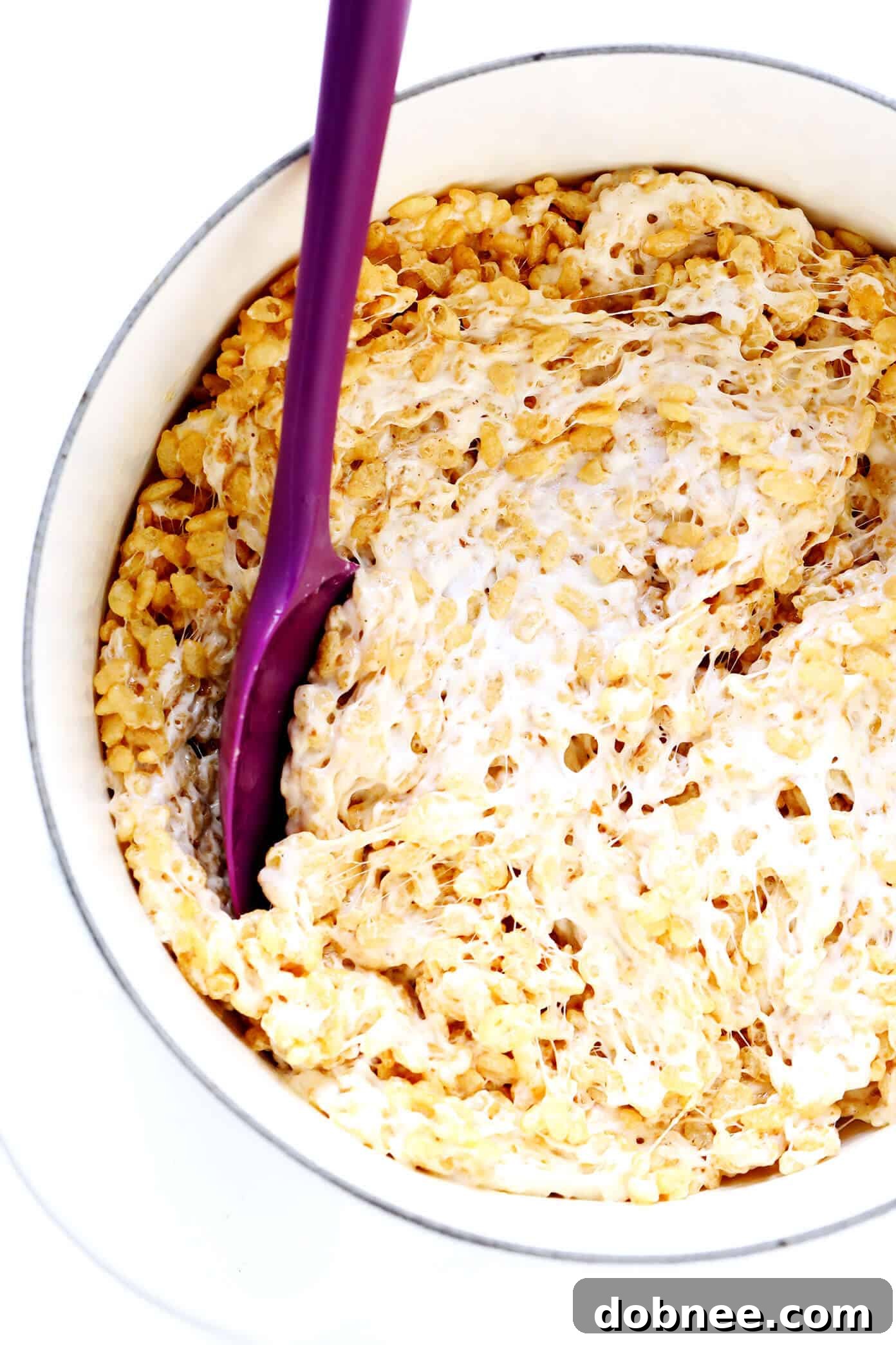 Stirring Rice Krispie Treats mixture in a large stockpot with browned butter, toasted marshmallows, and Rice Krispies.