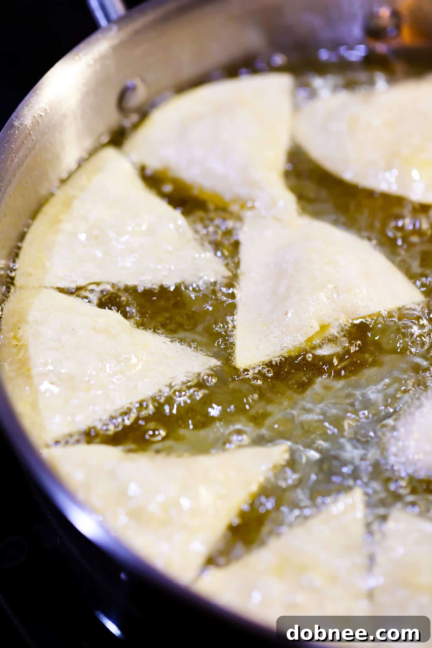 Close-up of corn tortilla wedges frying in hot oil, turning golden.