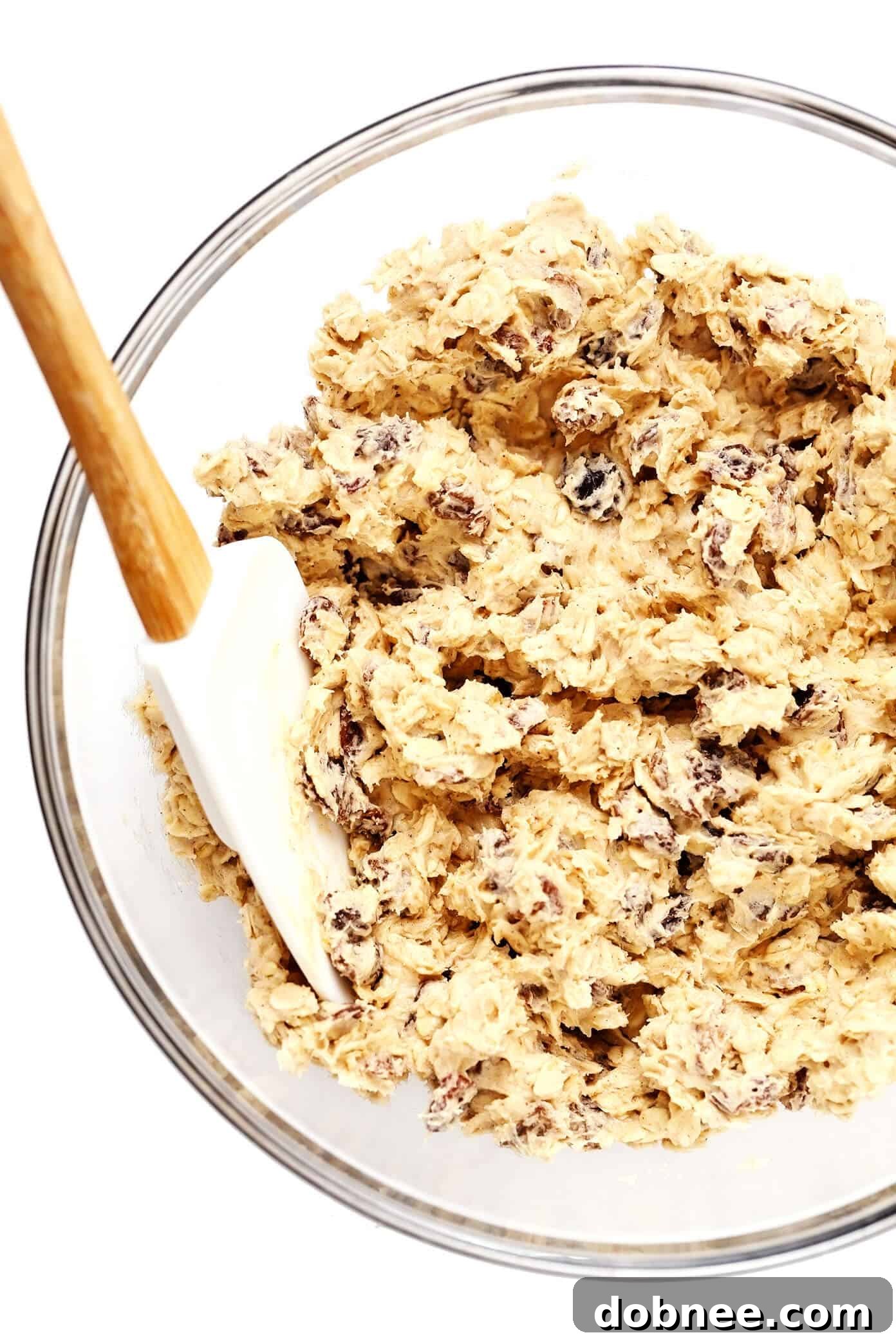 Oatmeal cookie dough being mixed with raisins, ready for baking on a wooden surface.