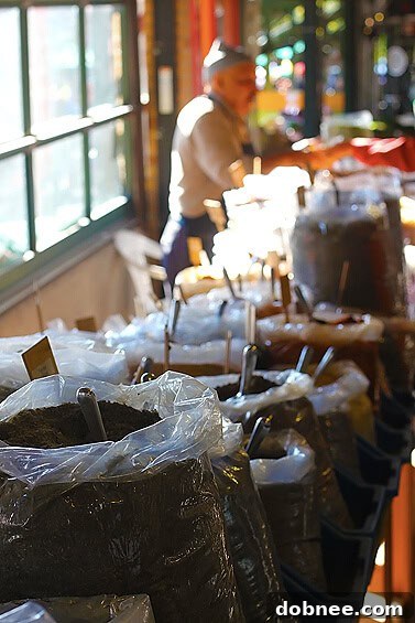 The Aromatic World of the Market's Spice Guy A vendor at a farmers market scooping spices for a customer from an array of colorful bulk spices in clear containers.