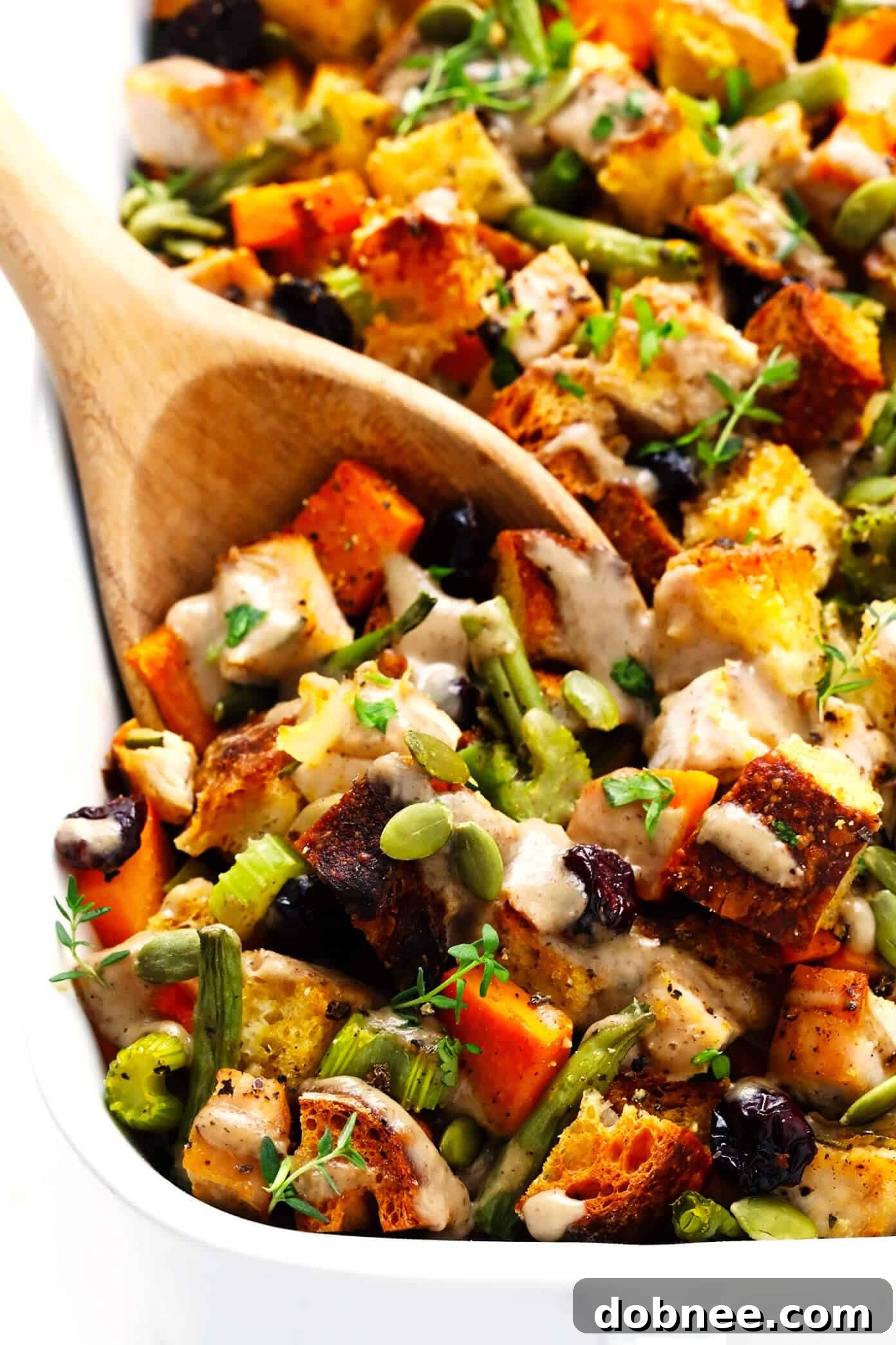 Thanksgiving Casserole Recipe Closeup with Serving Spoon. A hearty dish featuring turkey, herbed stuffing, green beans, sweet potatoes, and cranberries, topped with gravy.