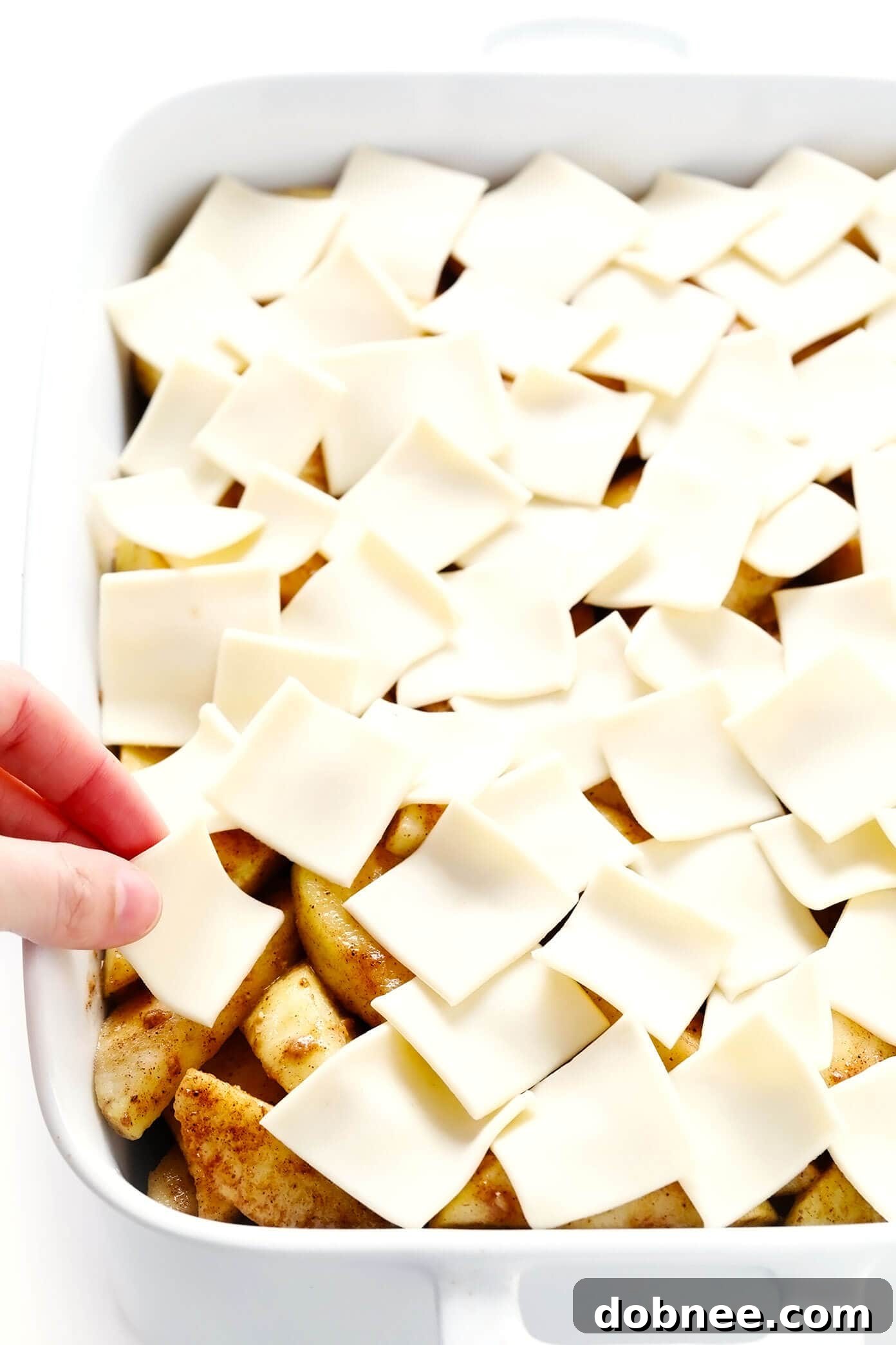 Layering puff pastry on apple pie filling for an easy pandowdy dessert. Preparing Apple Pandowdy: Layering puff pastry pieces over a seasoned apple filling in a baking dish.