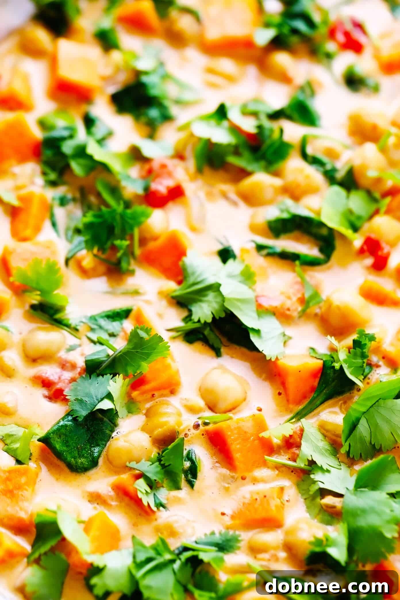 Close-up of creamy Sweet Potato Chickpea Coconut Curry in a sauté pan, showing tender sweet potatoes, chickpeas, and vibrant green spinach. A perfect vegan and gluten-free dinner.