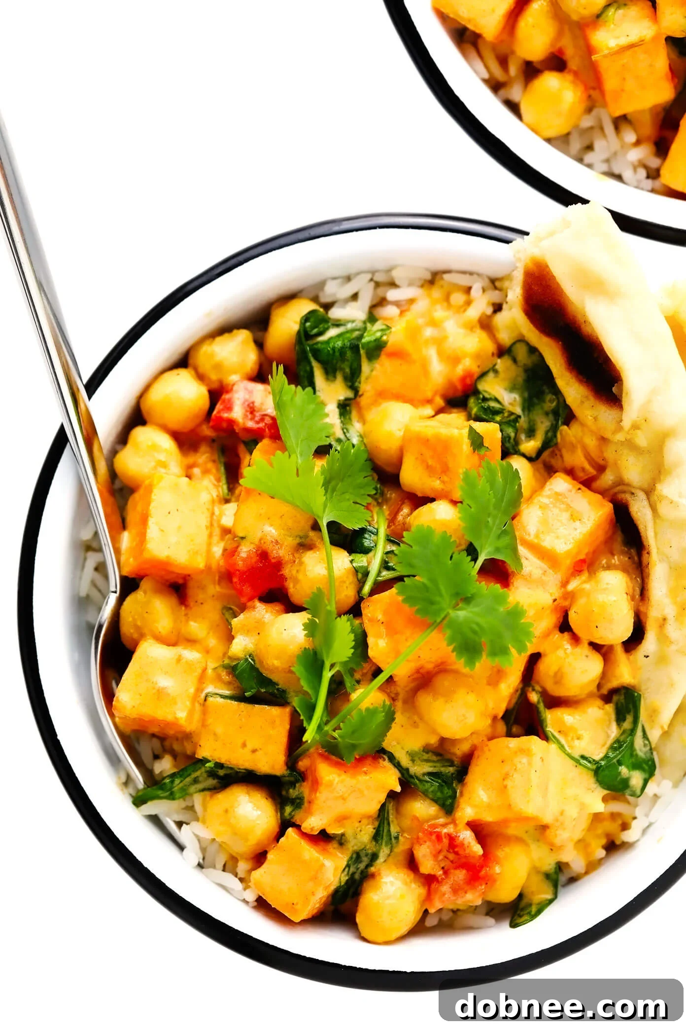 A bowl of Sweet Potato Chickpea Coconut Curry served with fluffy white rice and a piece of warm naan bread, garnished with fresh herbs. A perfect comforting vegan meal.