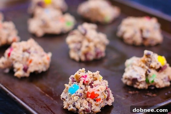 Close-up of freshly baked Granola M&M Cookies on a baking sheet, showing their golden edges and colorful M&M's.