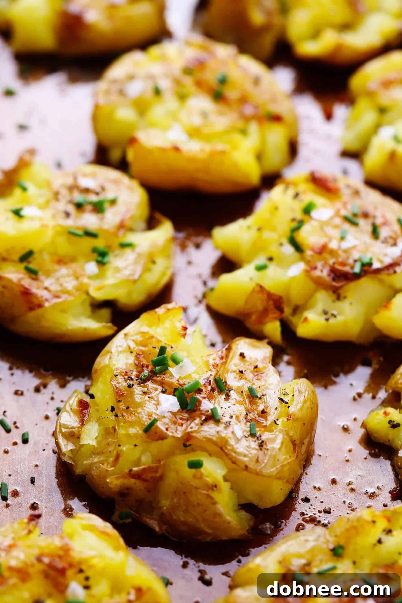 A close-up shot of golden-brown garlic smashed potatoes on a baking sheet, showcasing their crispy edges and tender texture, garnished with fresh herbs.