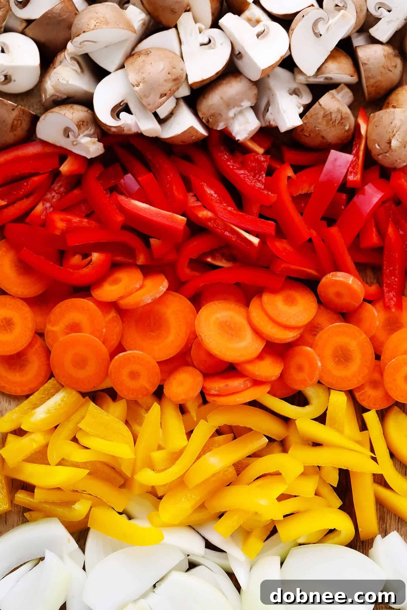 Assortment of fresh rainbow vegetables including mushrooms, bell peppers, carrots, and onions, prepped for Thai Chicken Curry.