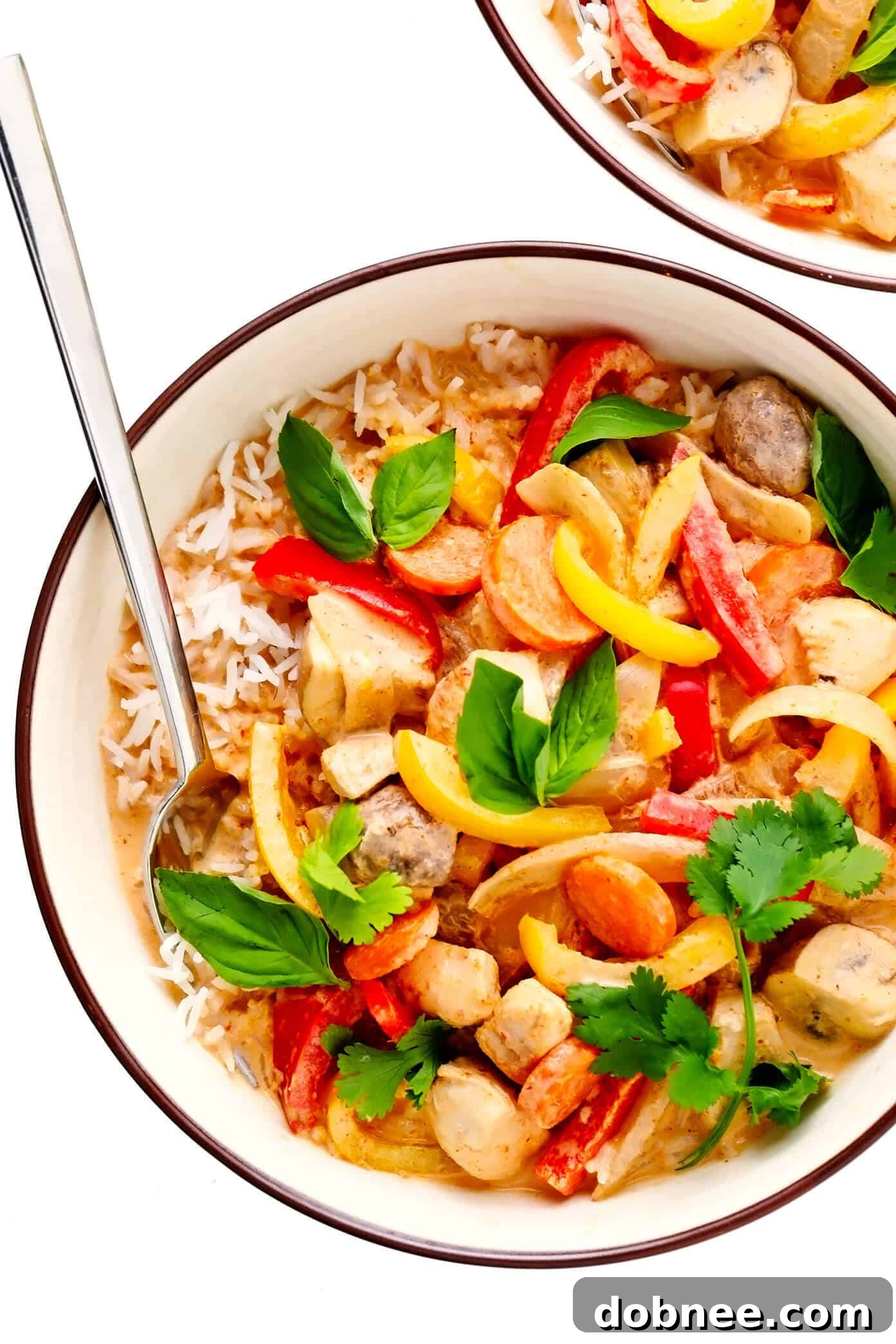 A vibrant bowl of Thai Chicken Curry garnished with fresh cilantro and lime wedges, served alongside rice.