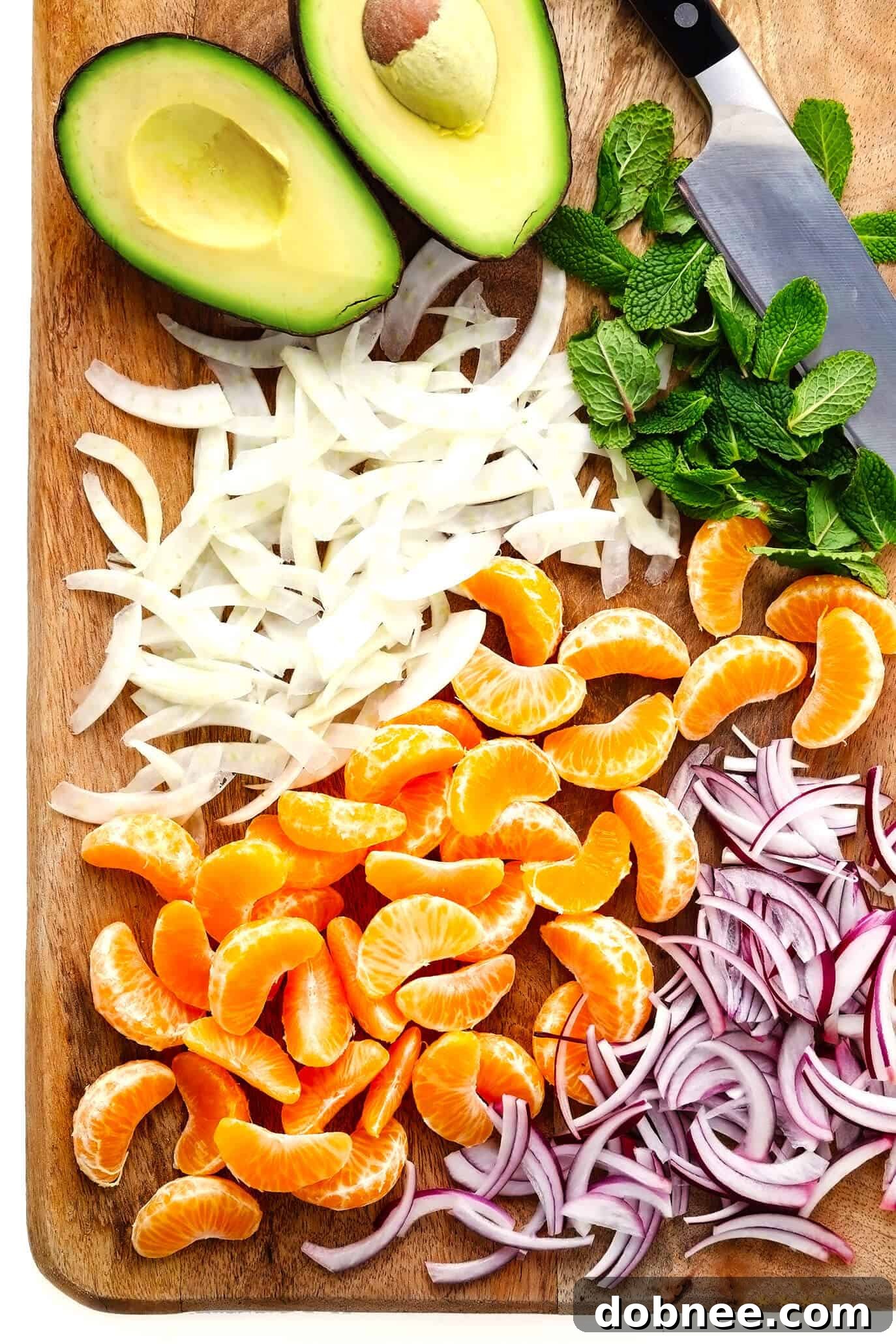 Fresh ingredients for Orange, Fennel and Avocado Salad arranged on a cutting board, including clementines, avocado, fennel, red onion, and mint.