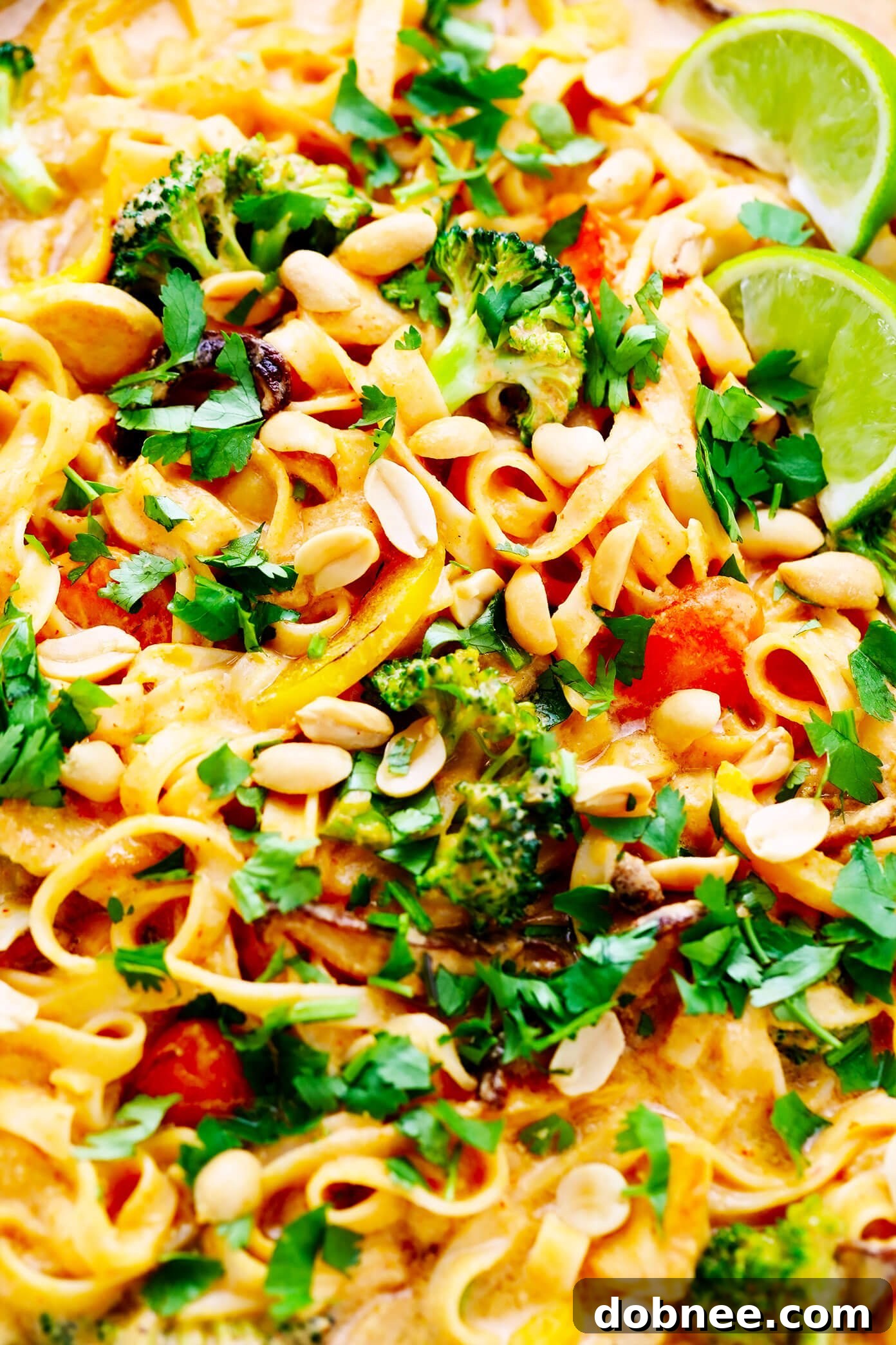 A close-up view of the Saucy Thai Curried Peanut Noodles, showcasing the rich texture of the sauce, intertwined with noodles and vegetables, garnished with fresh lime and cilantro.