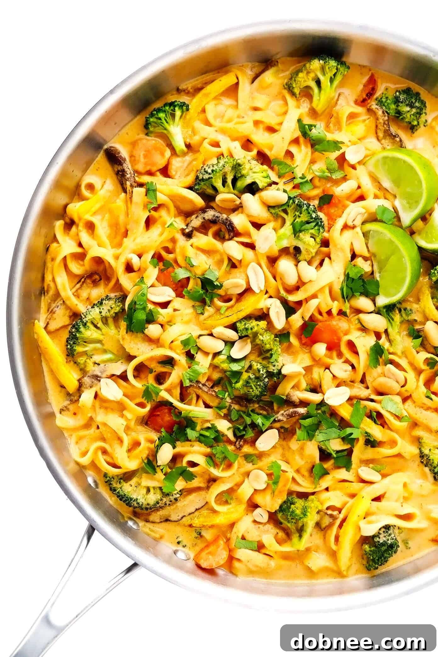 Thai Coconut Curry Peanut Noodles simmering in a large sauté pan, showcasing the rich, creamy sauce coating the ingredients.