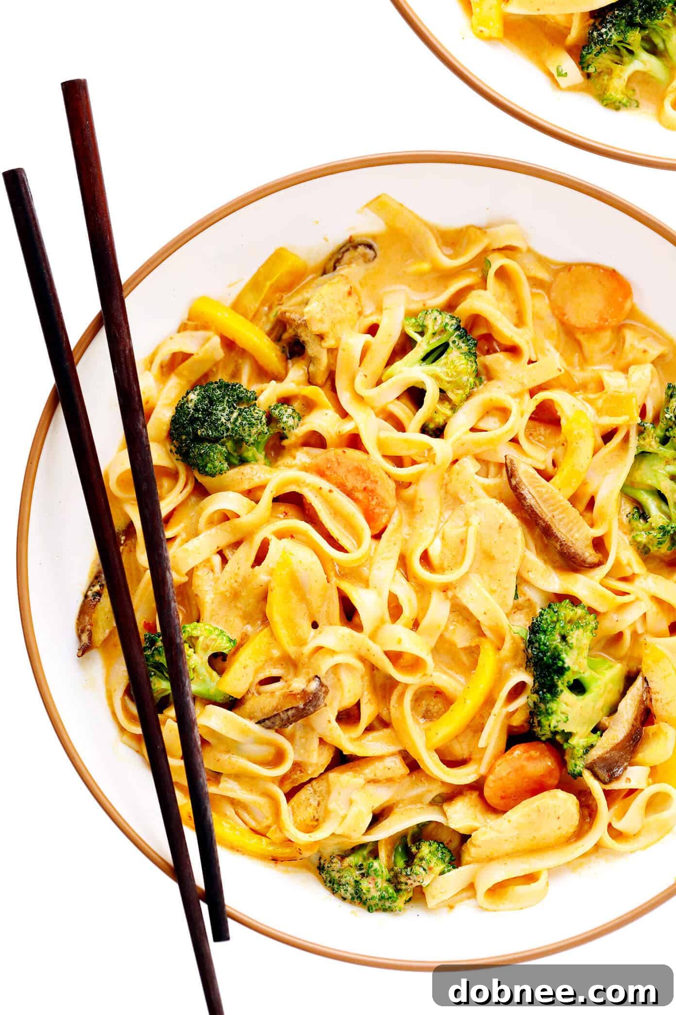 A beautifully plated bowl of Saucy Thai Curried Peanut Noodles with chicken, garnished with vibrant green cilantro and a fresh lime wedge, ready to be enjoyed.