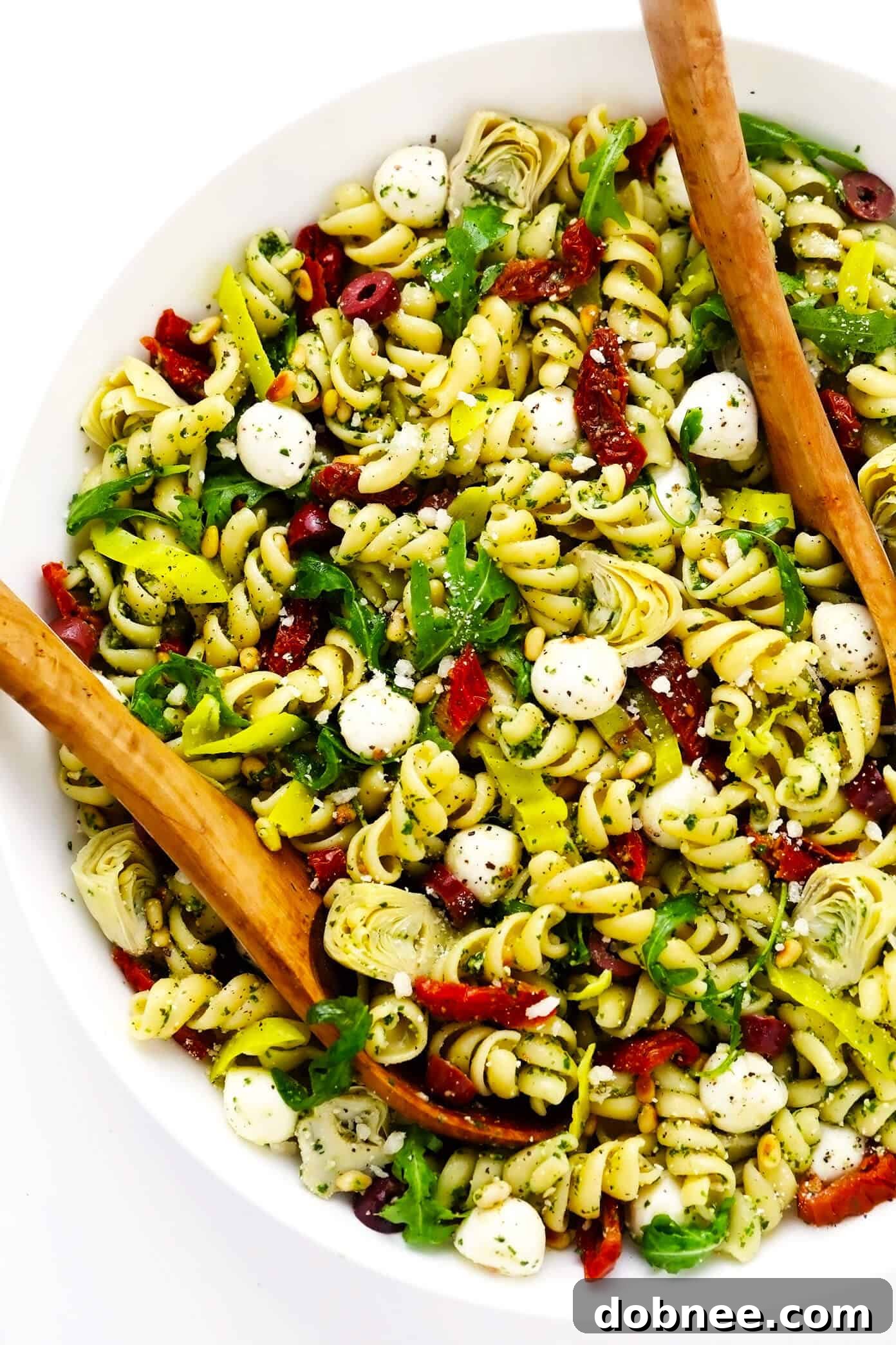 Pesto Pasta Salad, loaded with artichoke hearts, arugula, mozzarella, pepperoncini, Kalamata olives, pine nuts, and Parmesan. An easy vegetarian side dish for summer. Pesto Pasta Salad, a delicious Italian-inspired dish perfect for summer gatherings.