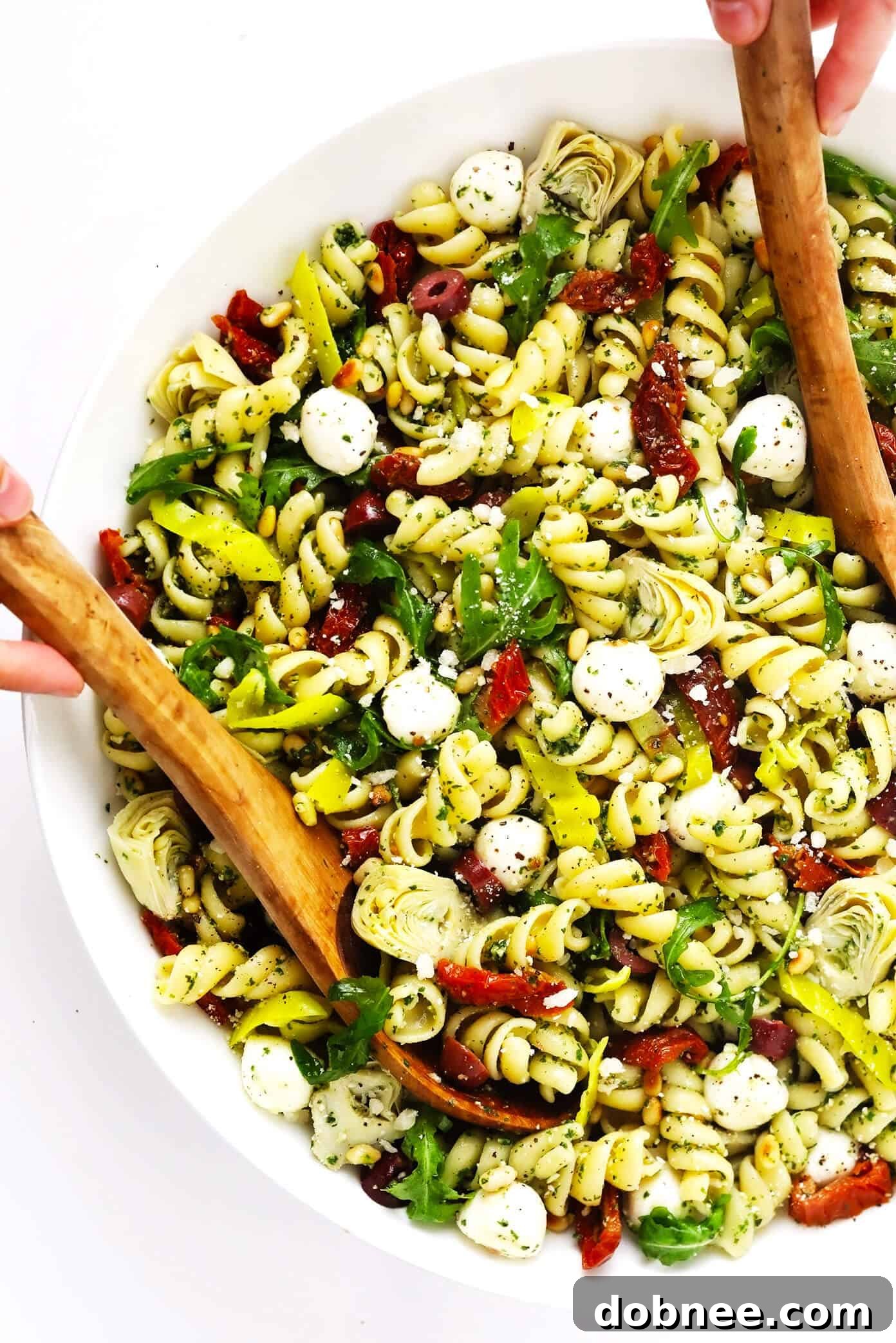 A vibrant and flavorful Italian Pesto Pasta Salad, featuring a colorful mix of fresh ingredients, ready to be served. Italian Pesto Pasta Salad in a large serving bowl with tongs.