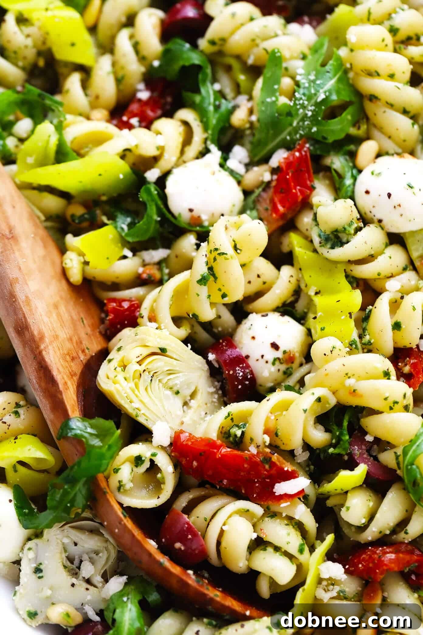 A close-up of the Pesto Pasta Salad showcasing the rich green pesto, tender pasta, and colorful Italian ingredients. Closeup view of Pesto Pasta Salad, showing the texture and vibrant ingredients.