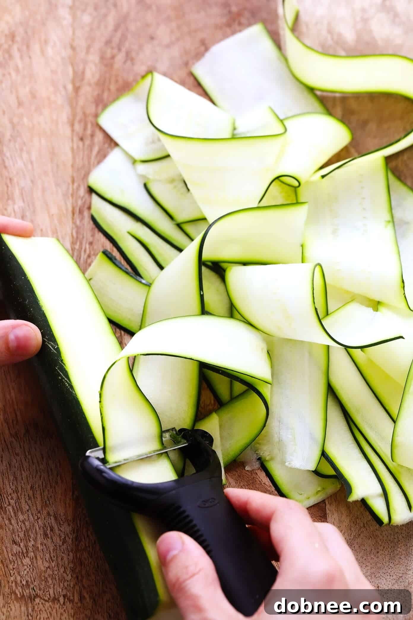 Detailed image showing how to thinly slice zucchini into long ribbons using a vegetable peeler